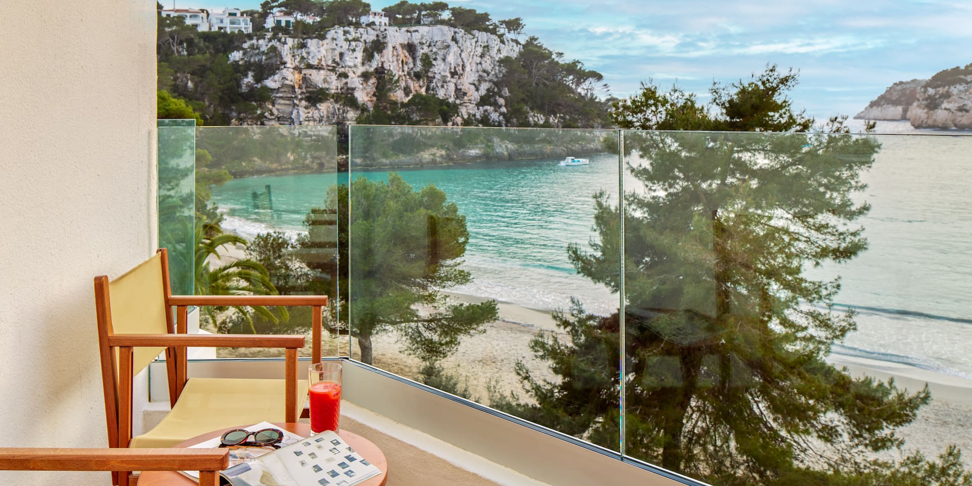 a chair and table with a glass fence overlooking a beach