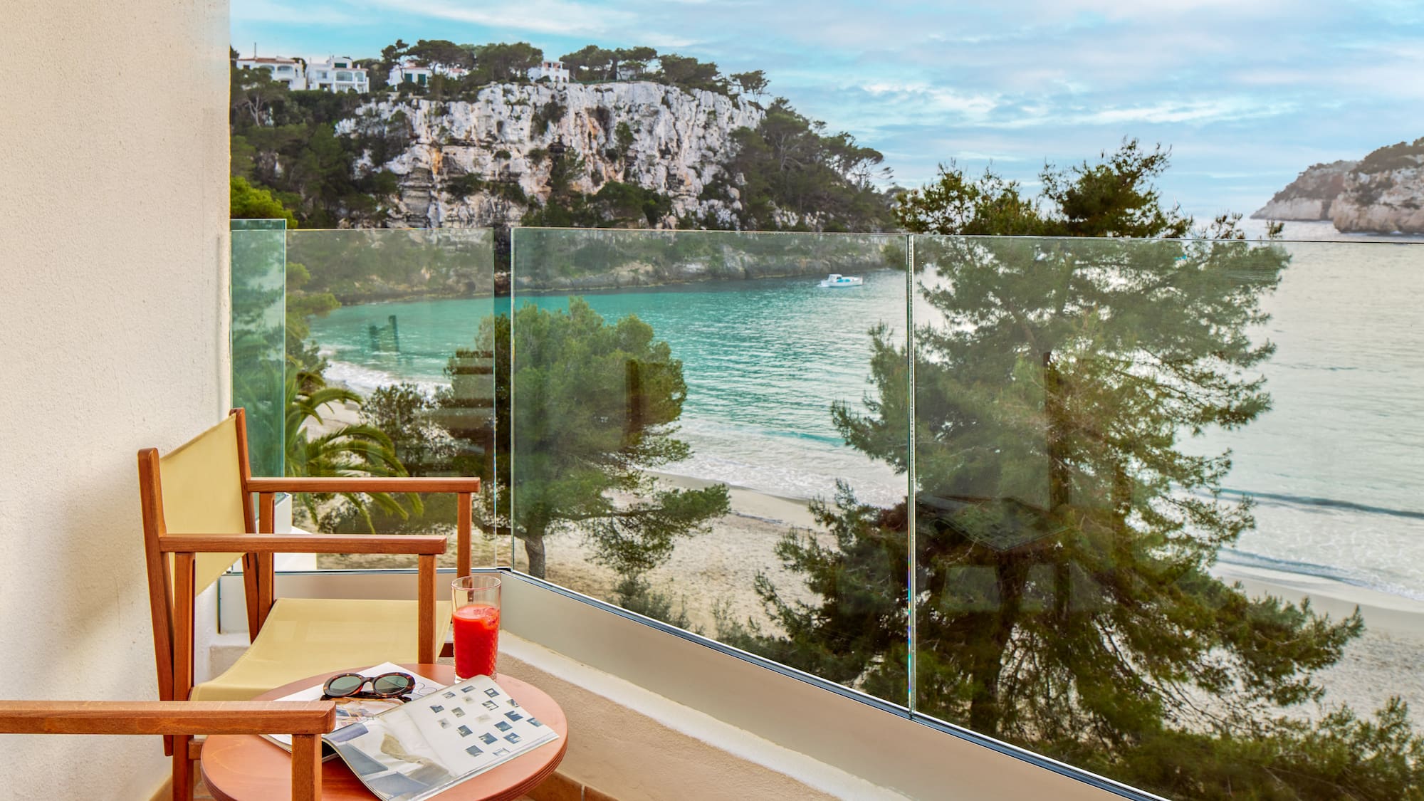 a chair and table with a glass fence overlooking a beach