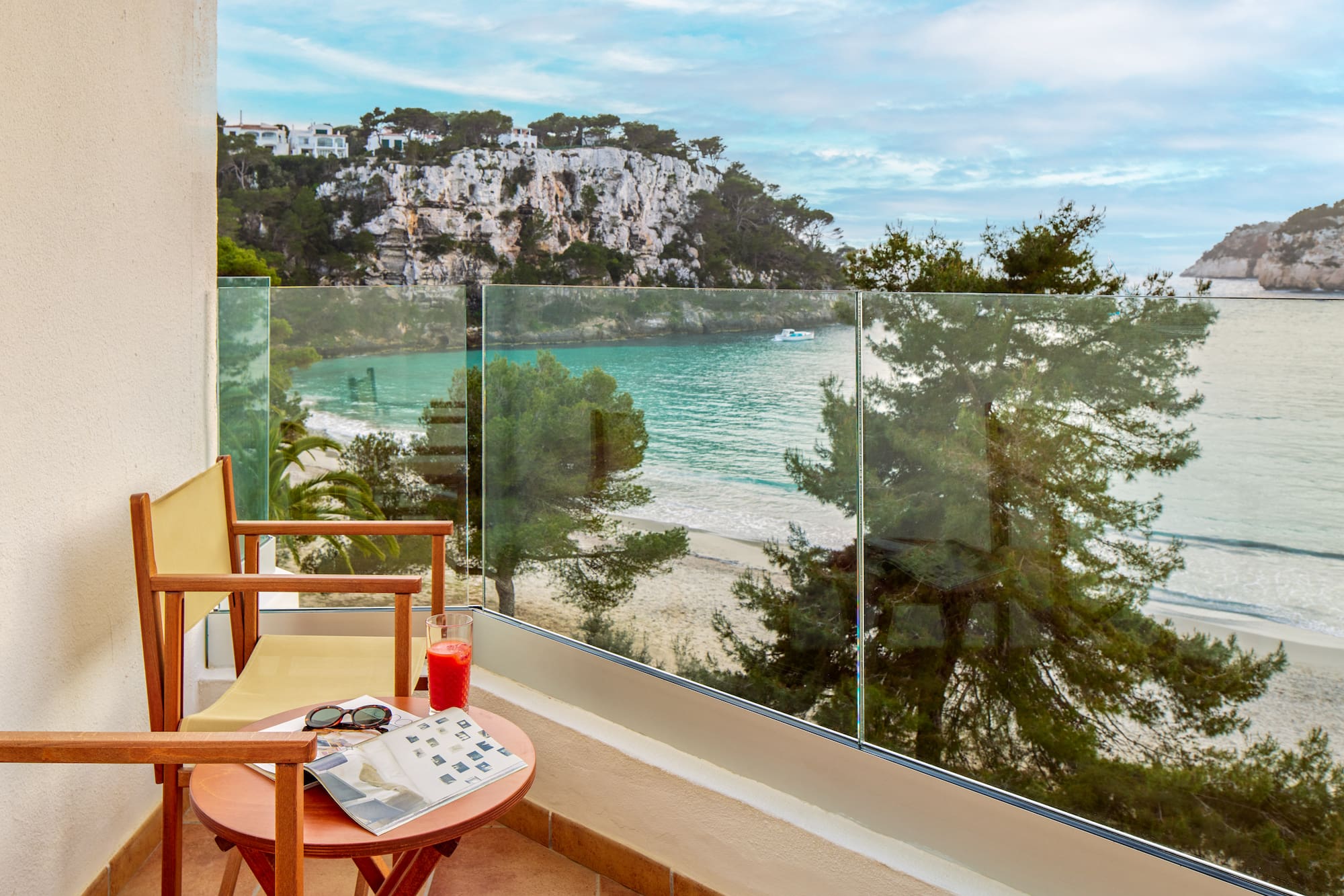 a chair and table with a glass fence overlooking a beach
