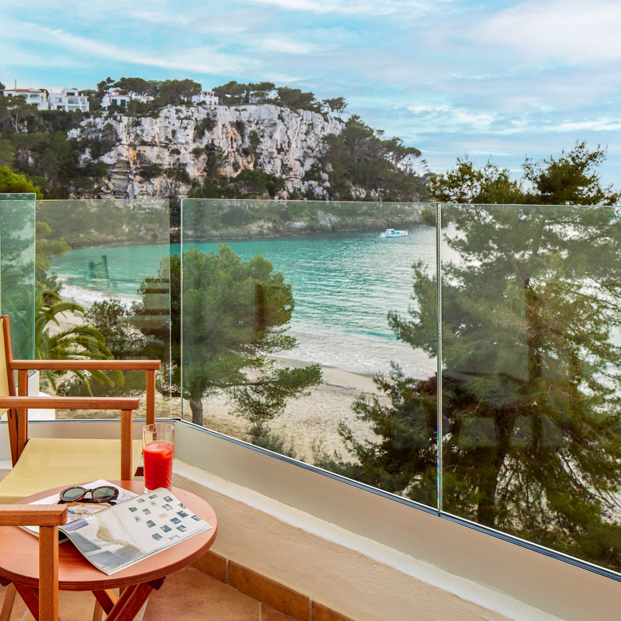 a chair and table with a glass fence overlooking a beach