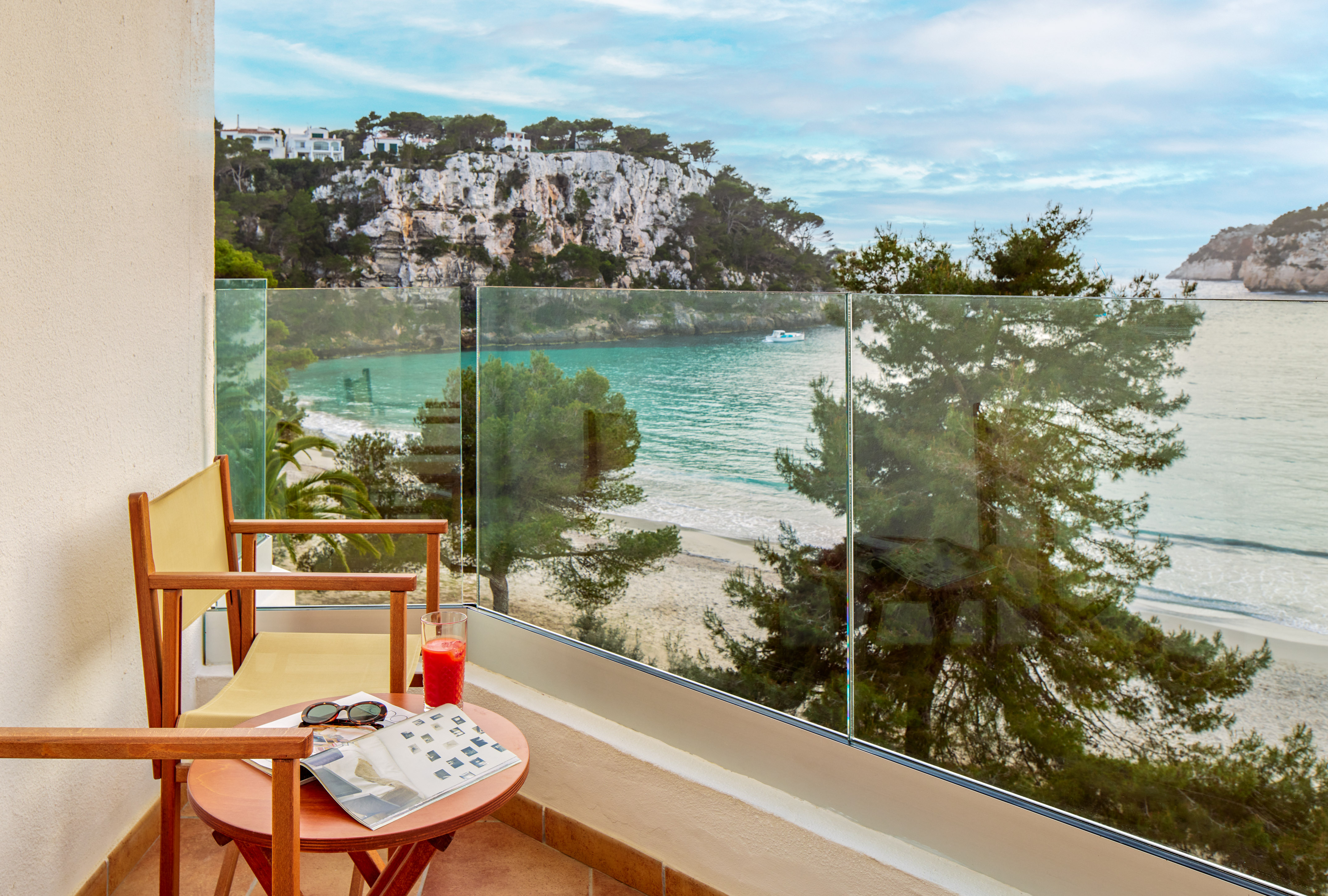 Balcony overlooking turquoise sea, sandy beach, and green cliffs.