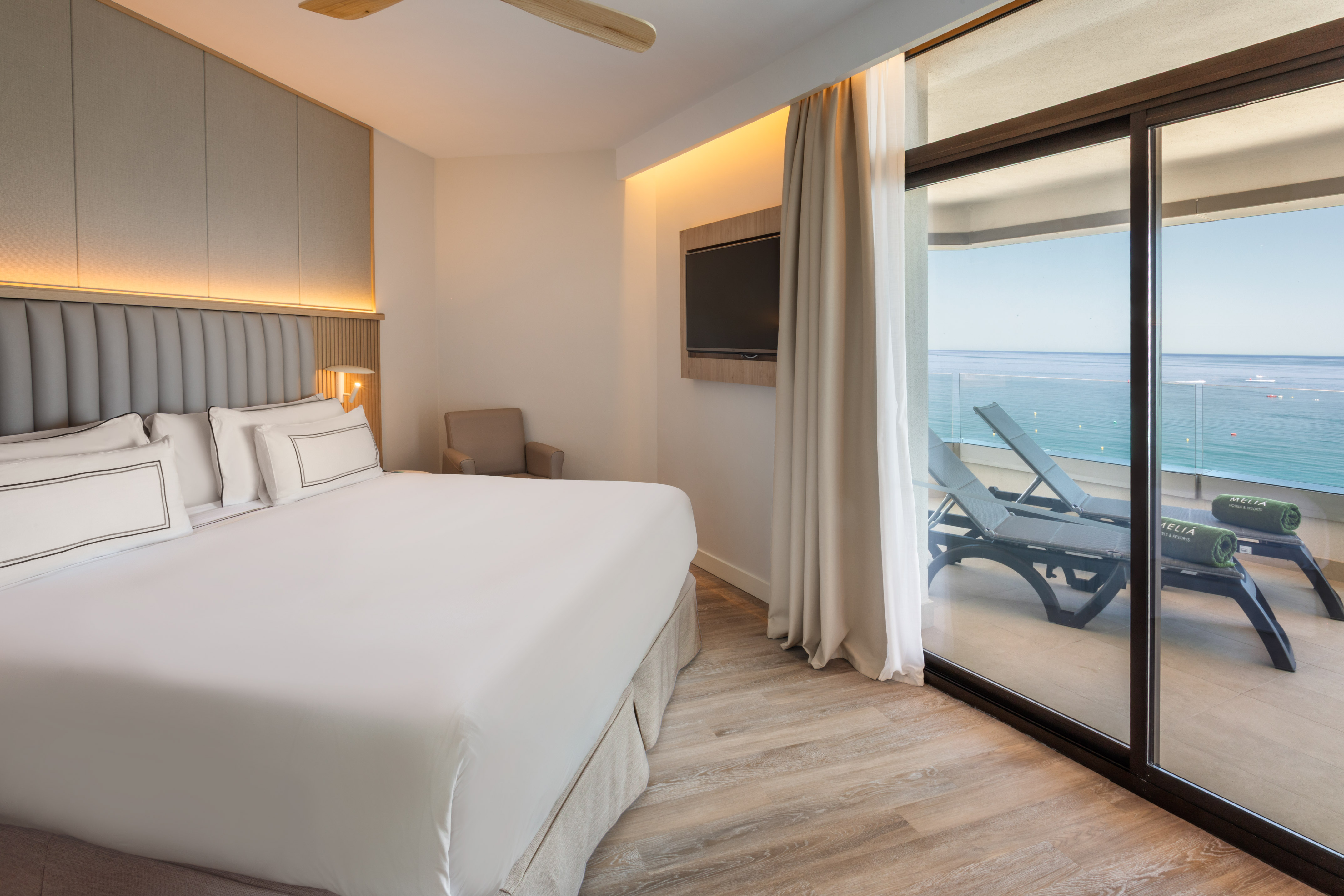 Luxury hotel bedroom with ocean view balcony and lounge chairs.