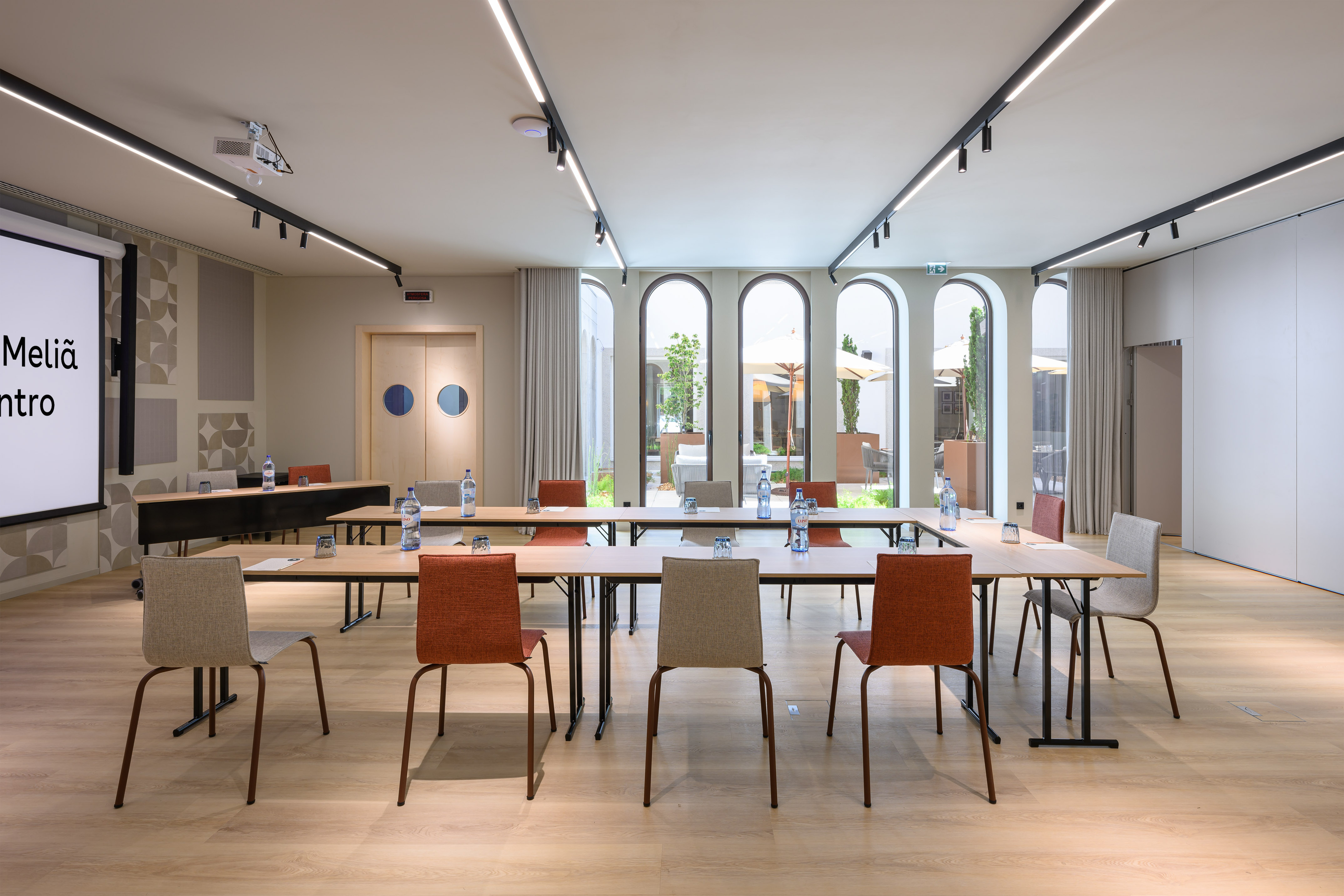 Meliá conference room with U-table setup, projector screen, and arched windows.