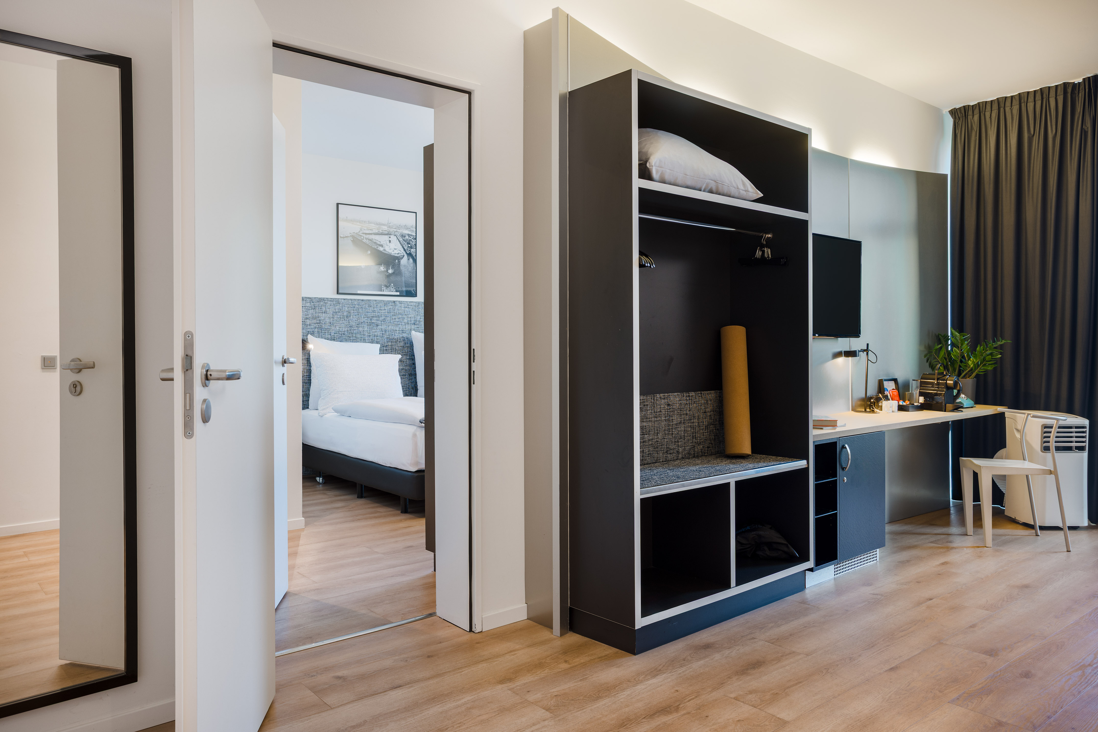 Modern hotel room interior: open wardrobe, work desk, adjoining bedroom.