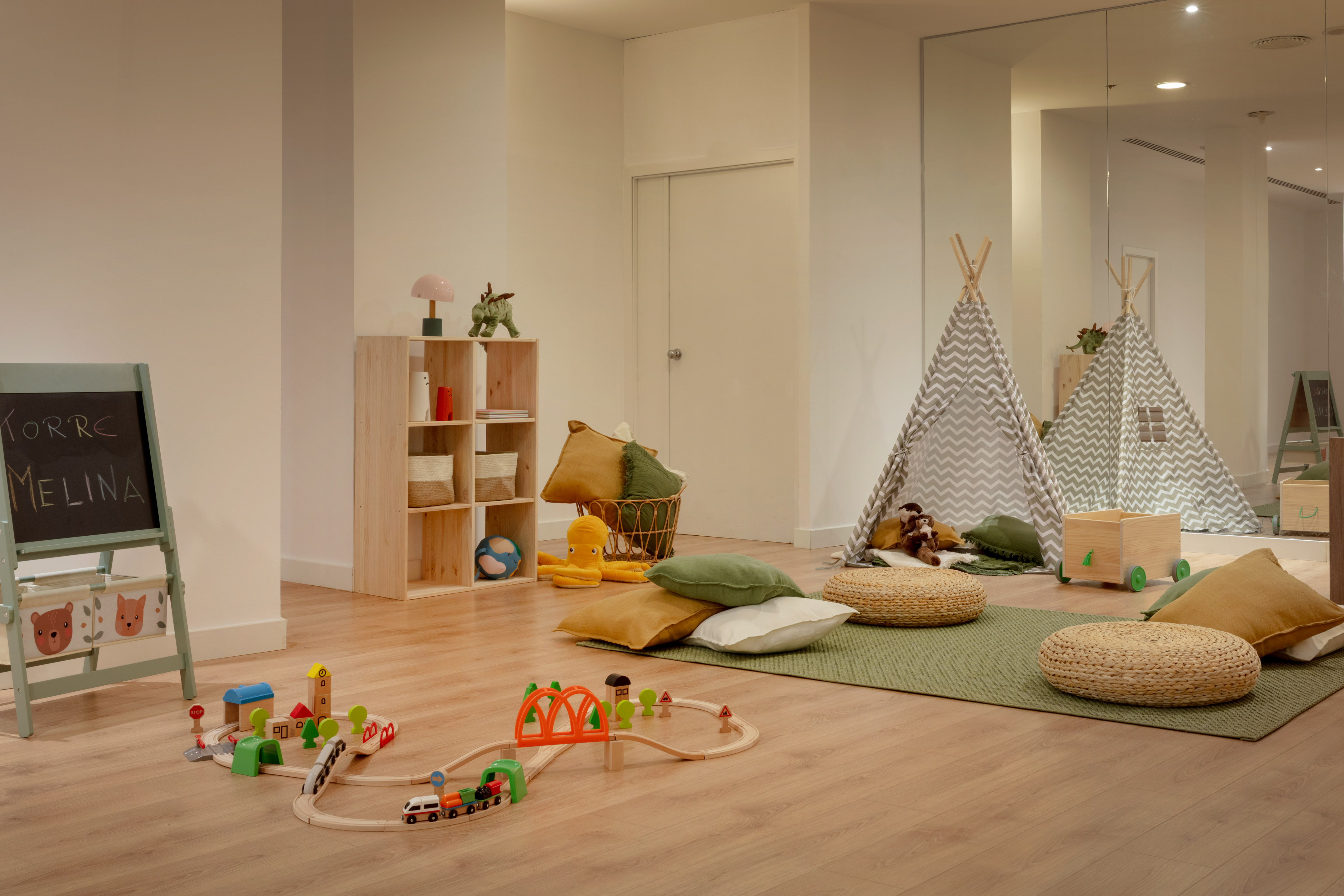 Cozy kids' playroom with wooden train set, teepee, cushions, and chalkboard.