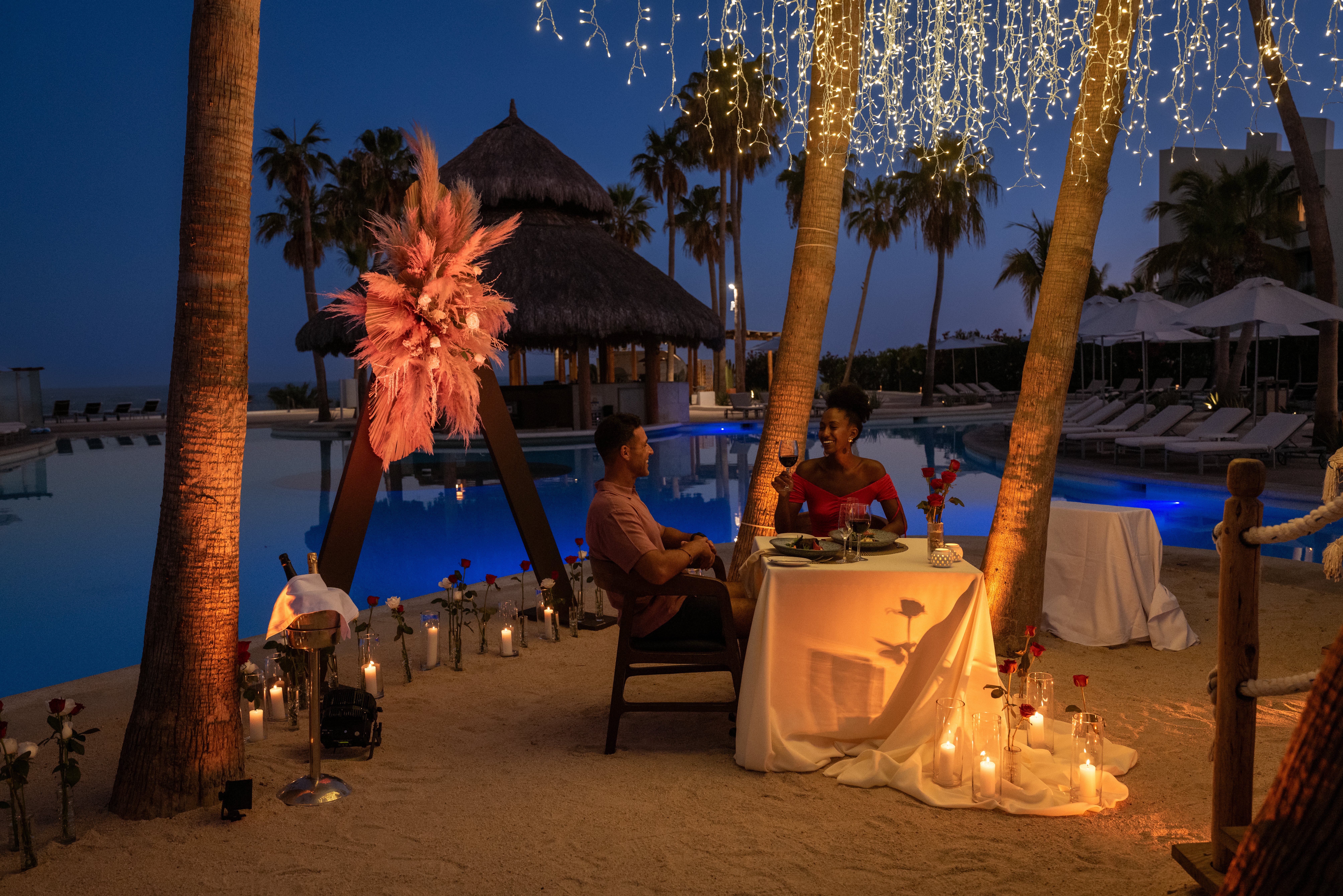 a man and woman sitting at a table under a pool with lights