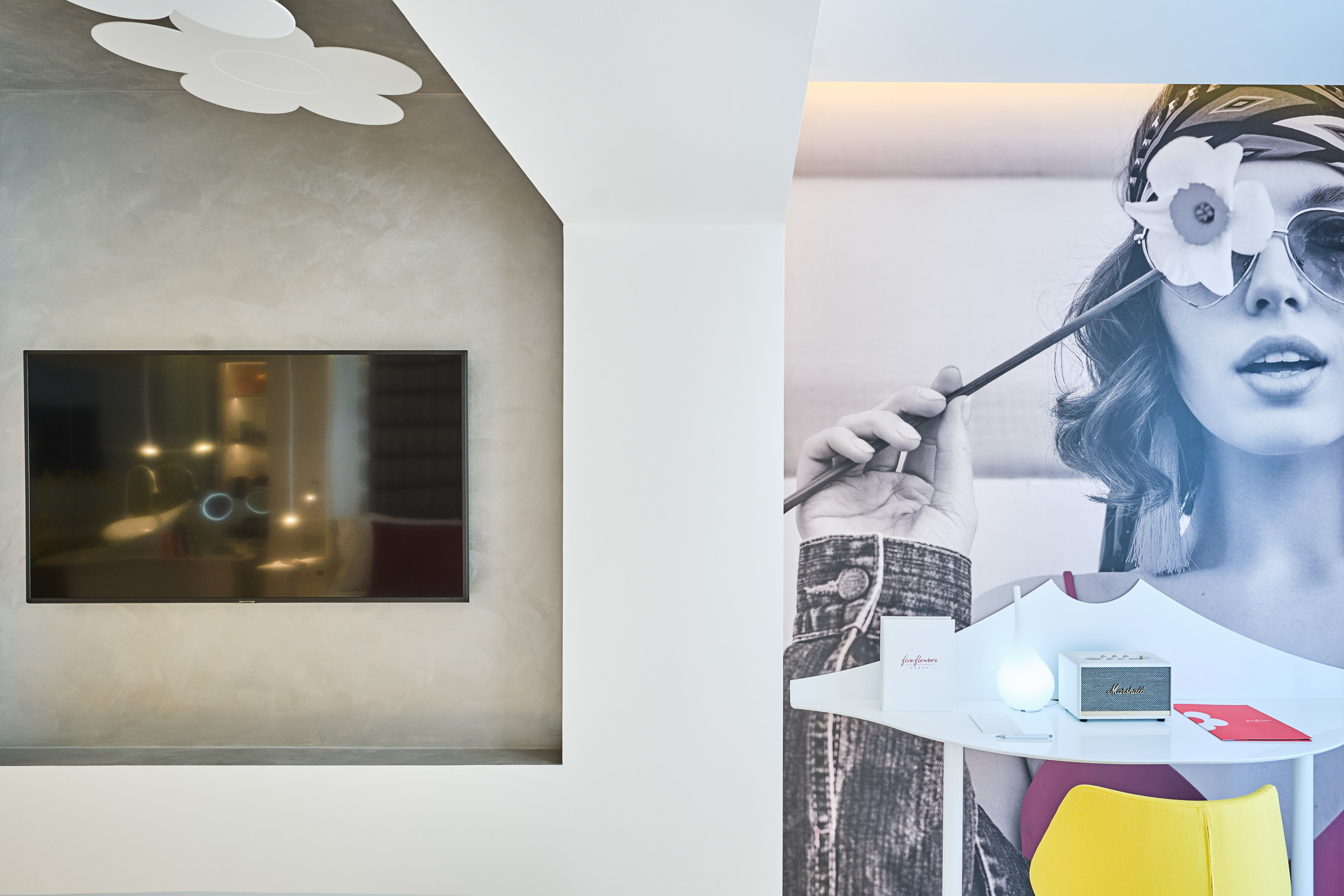 Modern room, TV, flower ceiling light, bohemian woman mural, desk with Marshall speaker.