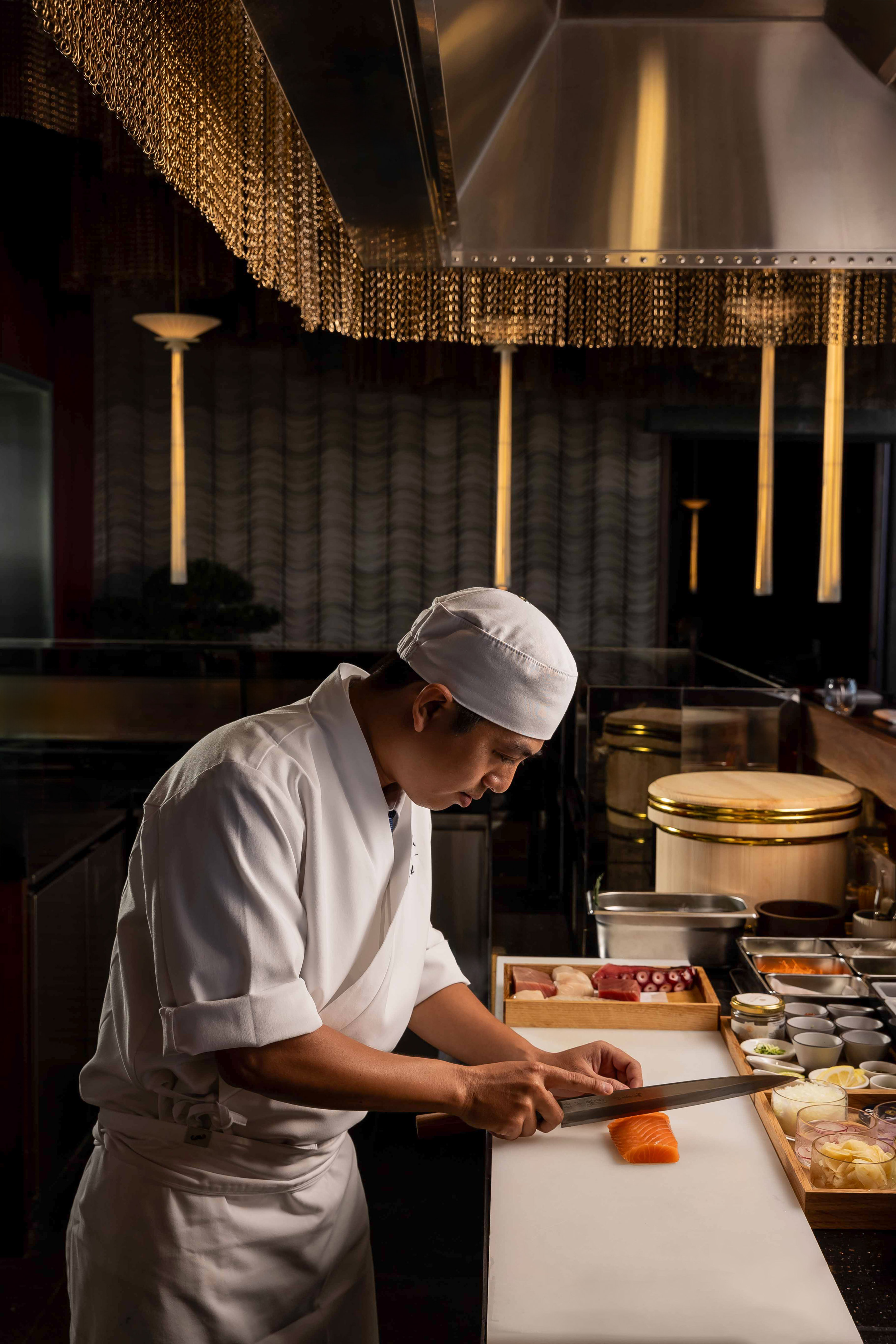 Professional sushi chef slicing salmon, surrounded by fresh Japanese ingredients.