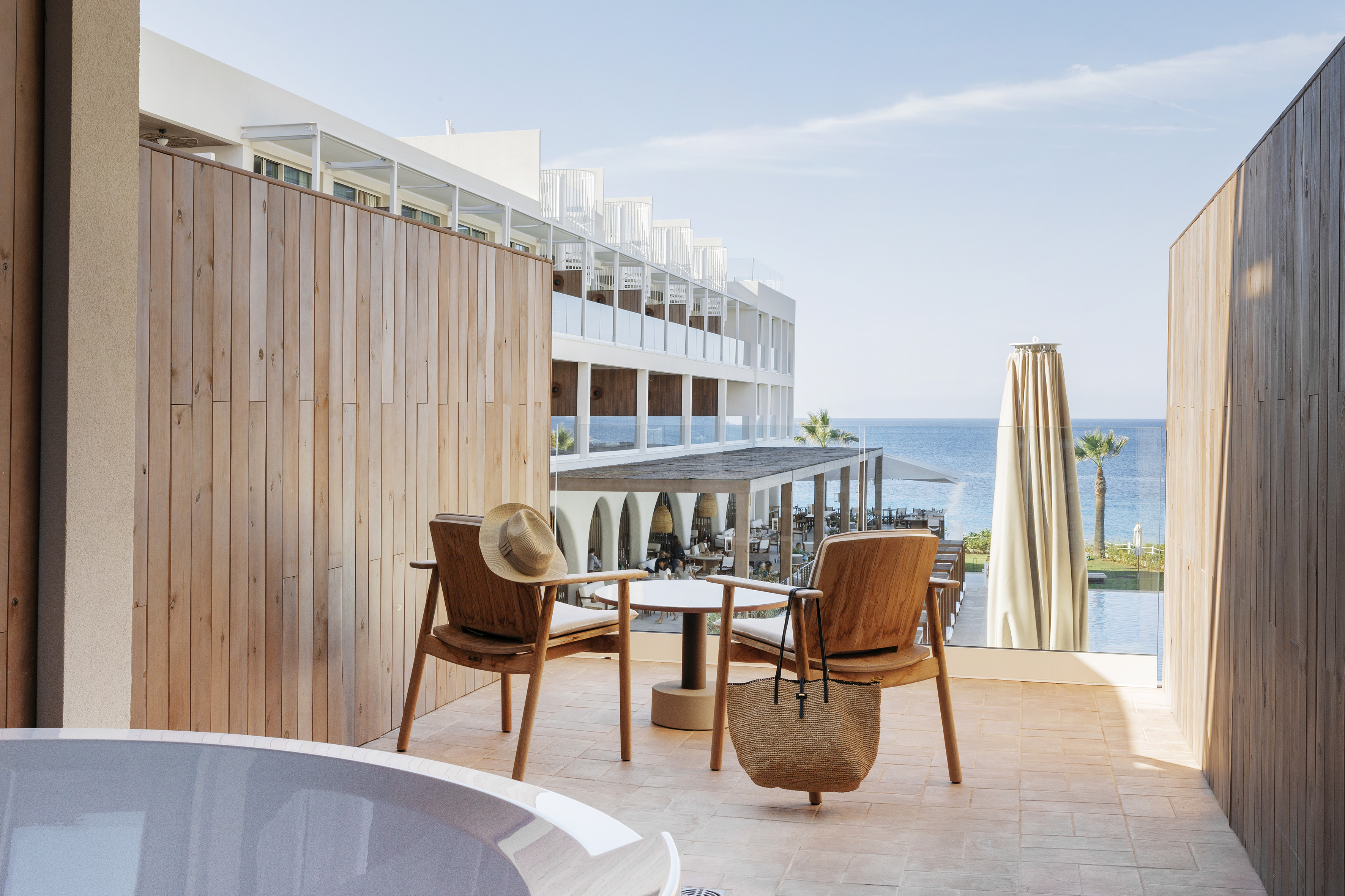 Resort balcony with wooden chairs, hot tub, and clear blue ocean view.