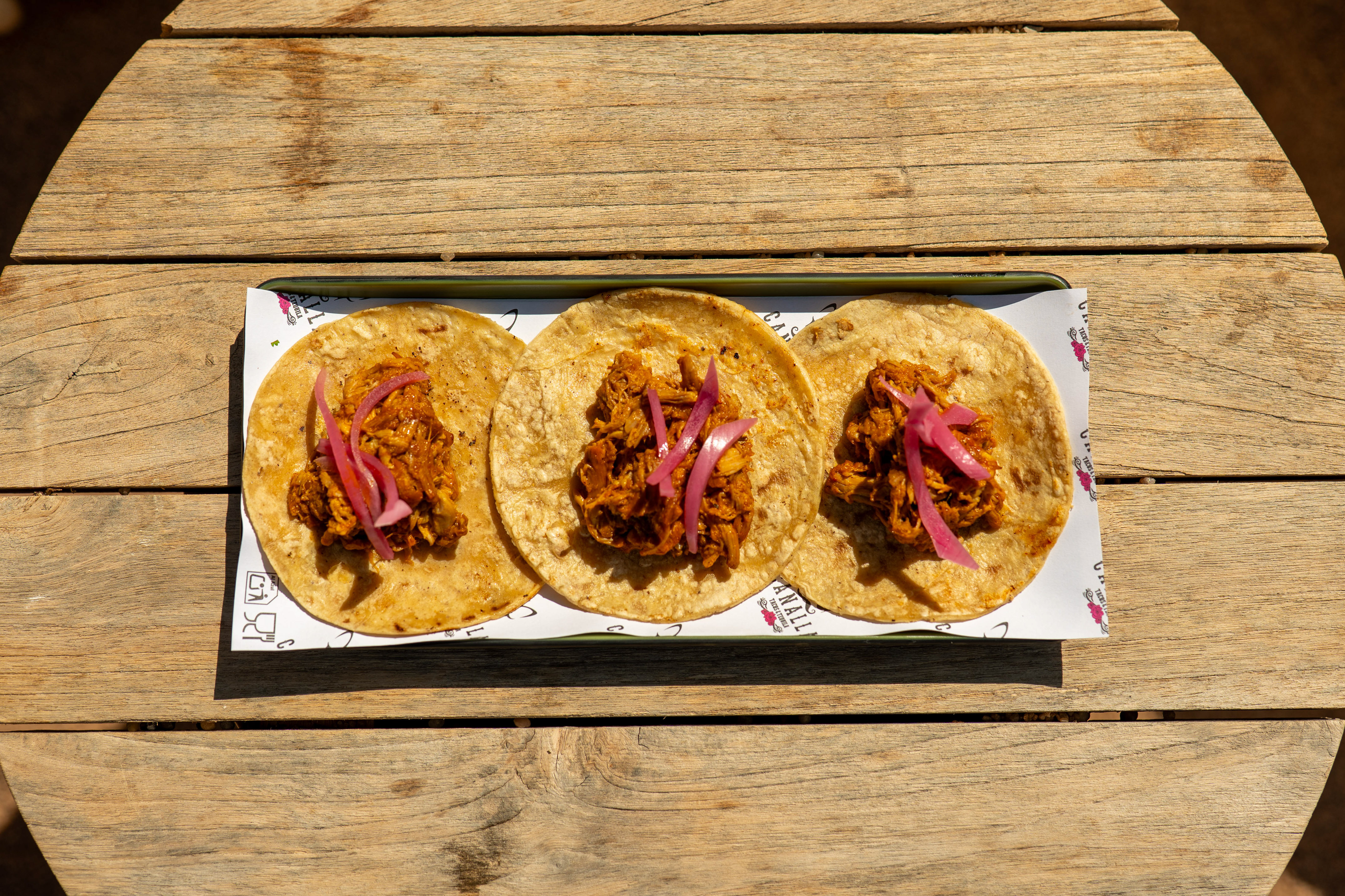Three cochinita pibil tacos with pickled red onions on a wooden table.