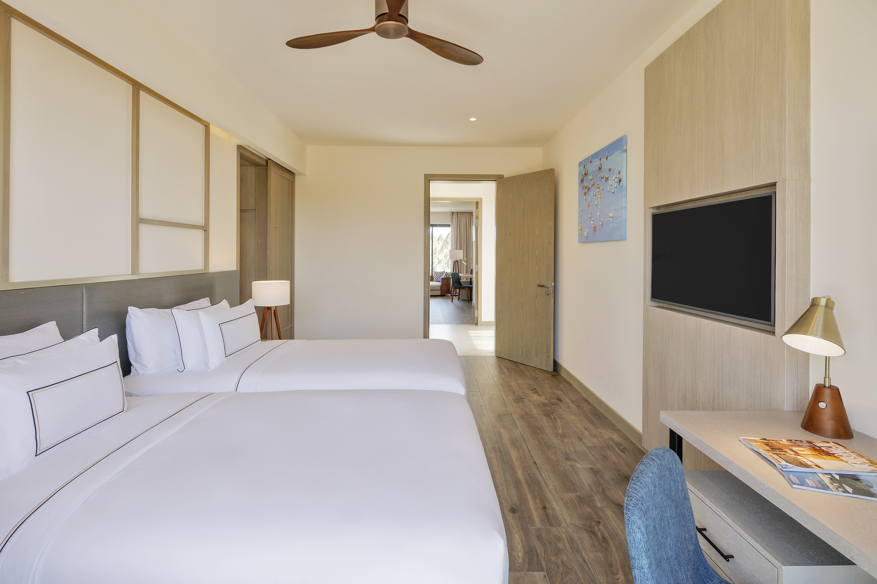 Modern hotel suite bedroom with two twin beds, wooden floor, TV, and desk.