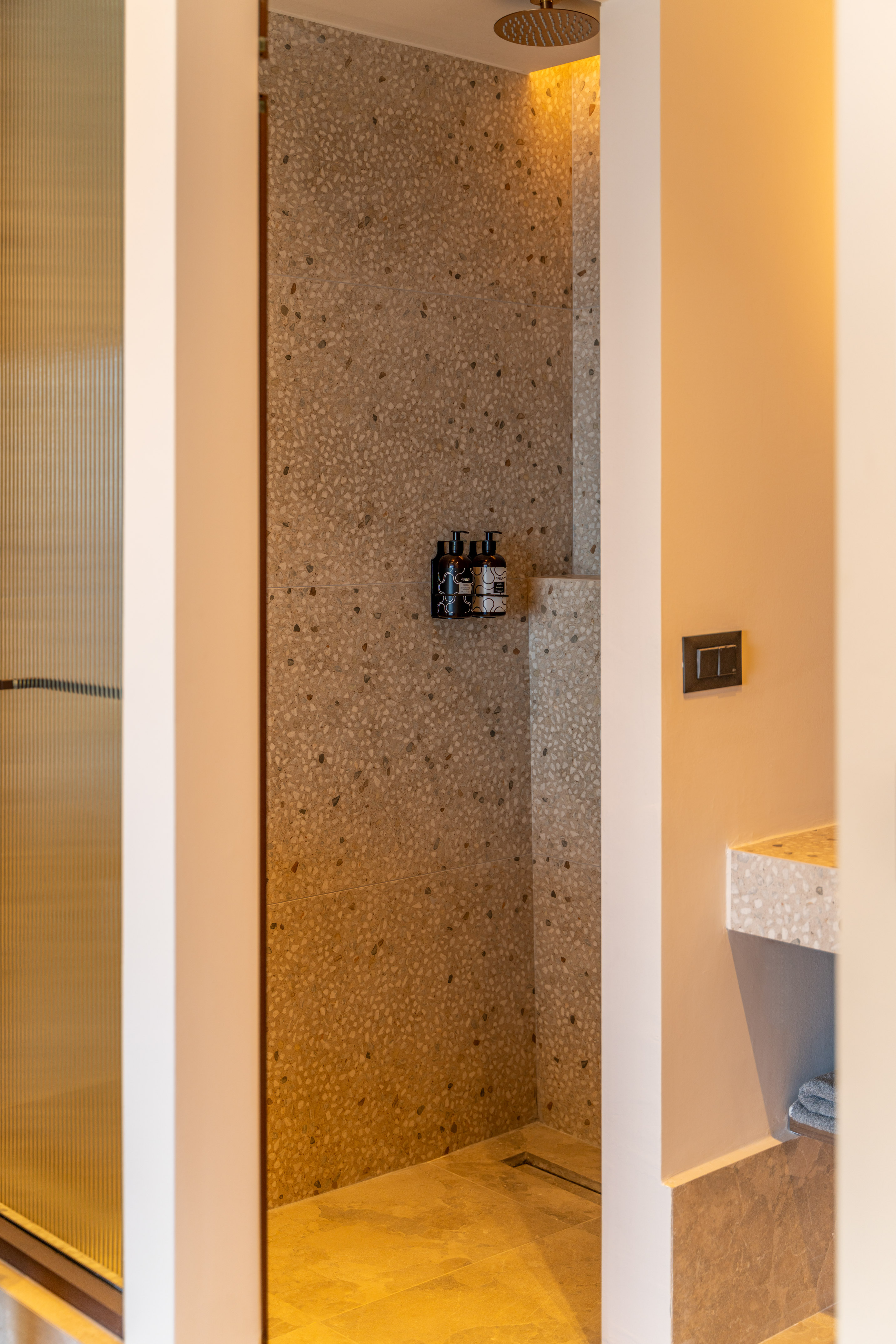 Stylish modern shower with speckled terrazzo walls and warm tiled floor.