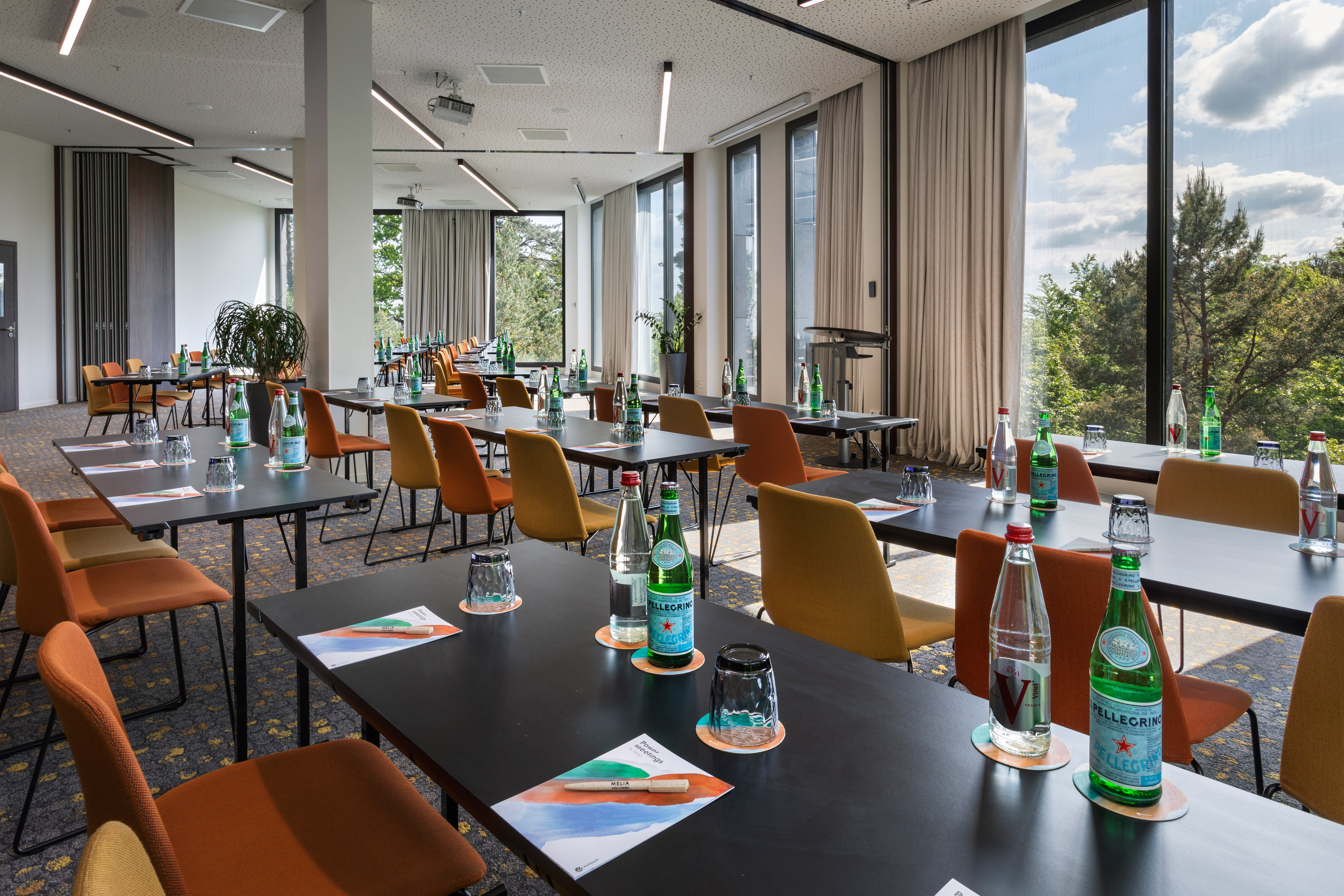 Spacious meeting room set with tables, chairs, water, and large windows.