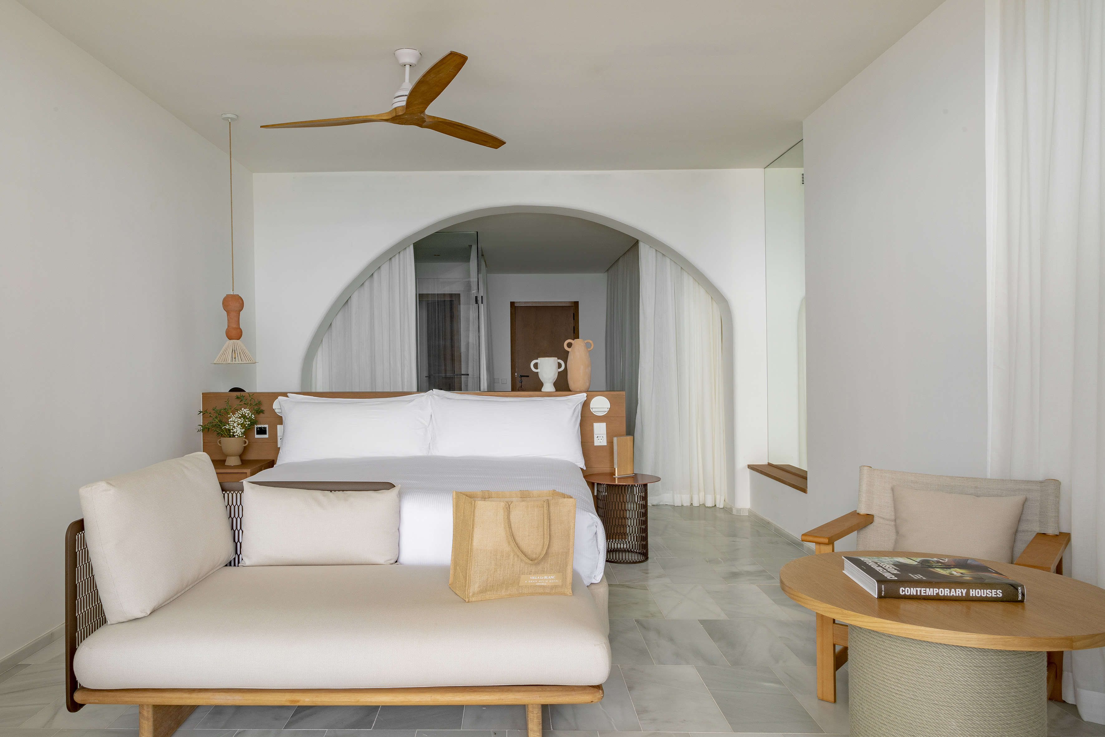 Contemporary resort bedroom with white bed, chaise lounge, and arched walls.