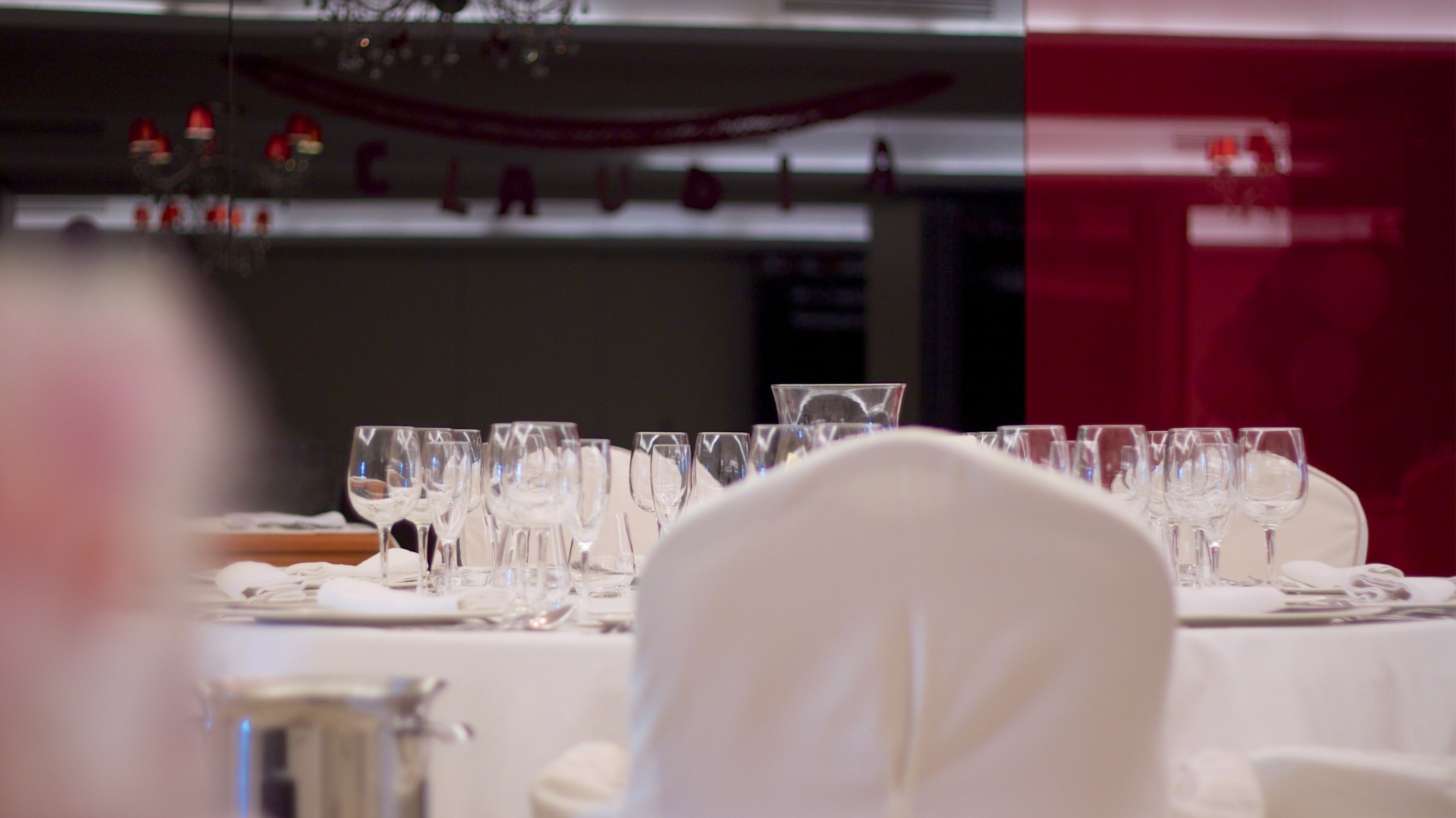 Red decor and 'Claudia' banner above set dining table with empty glasses.