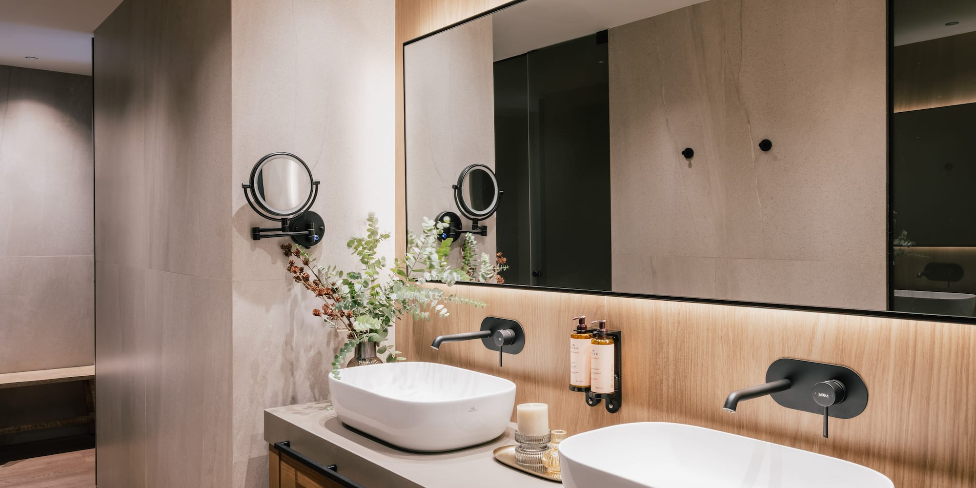 Modern bathroom double vanity with white vessel sinks, black faucets, backlit mirror.