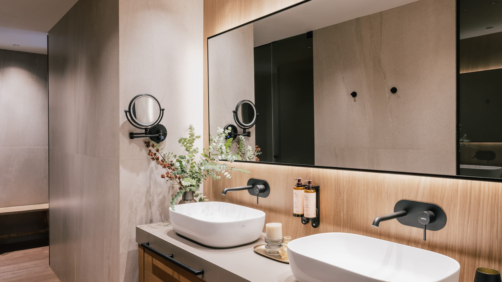 Modern bathroom double vanity with white vessel sinks, black faucets, backlit mirror.