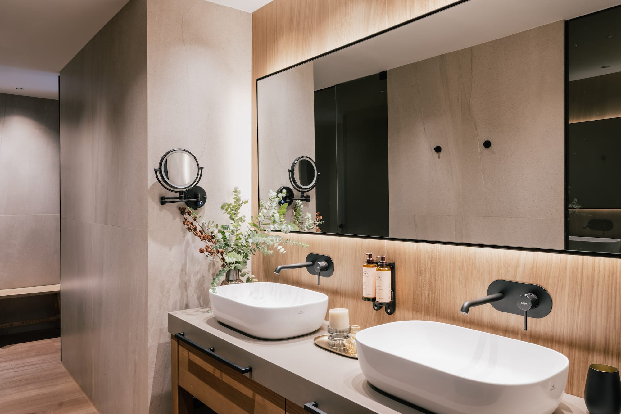 Modern bathroom double vanity with white vessel sinks, black faucets, backlit mirror.
