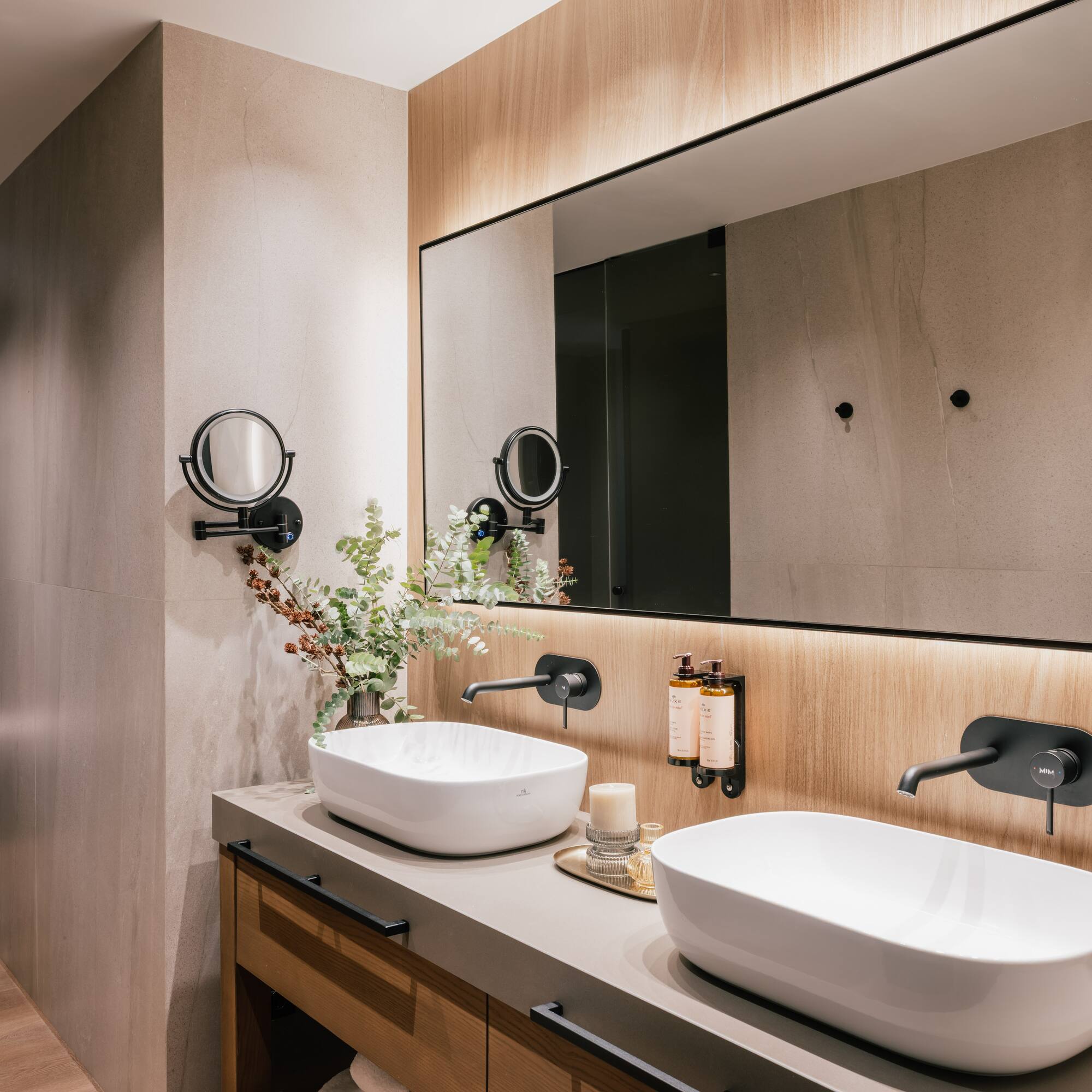 Modern bathroom double vanity with white vessel sinks, black faucets, backlit mirror.