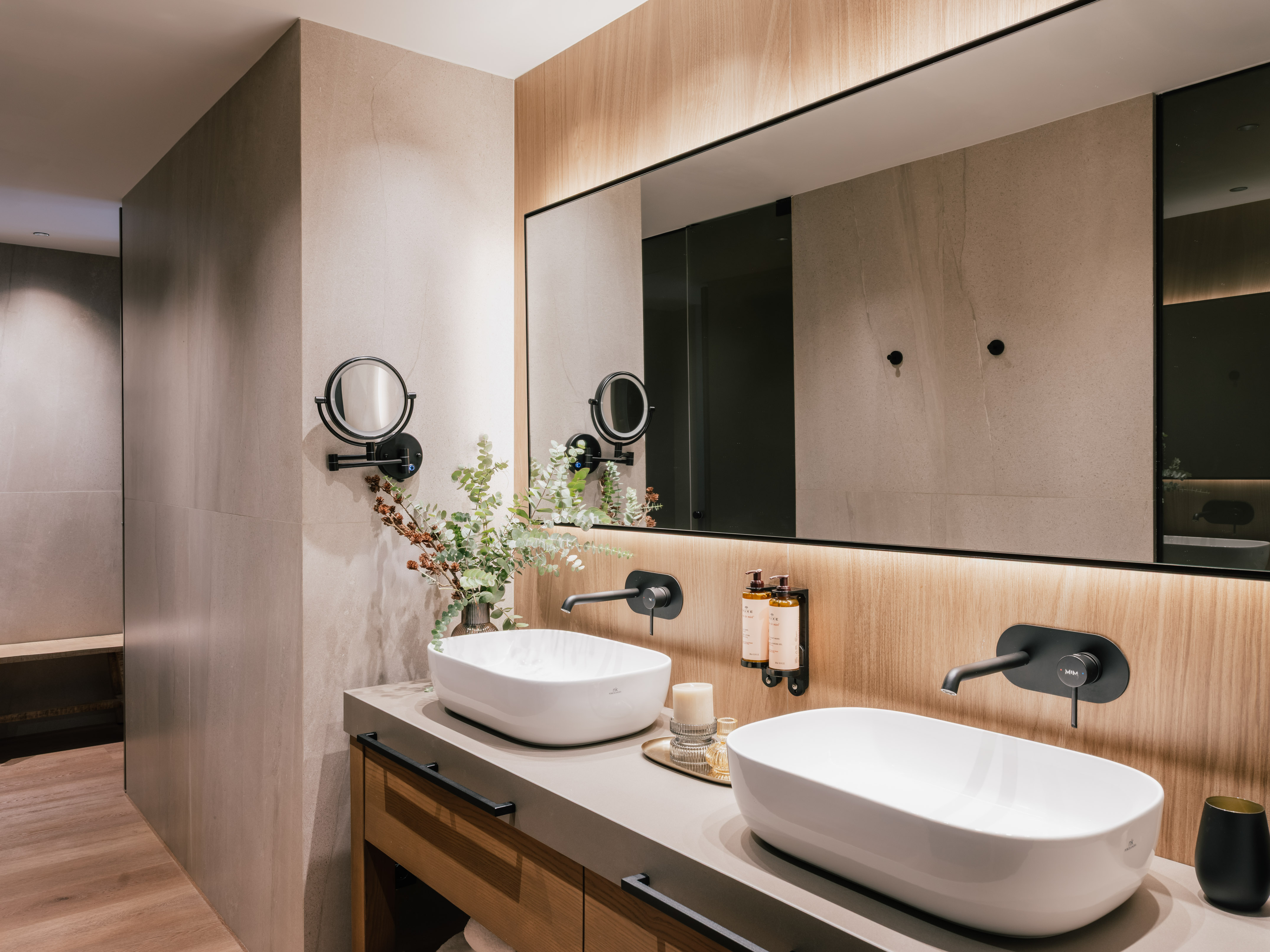 Modern bathroom double vanity with white vessel sinks, black faucets, backlit mirror.