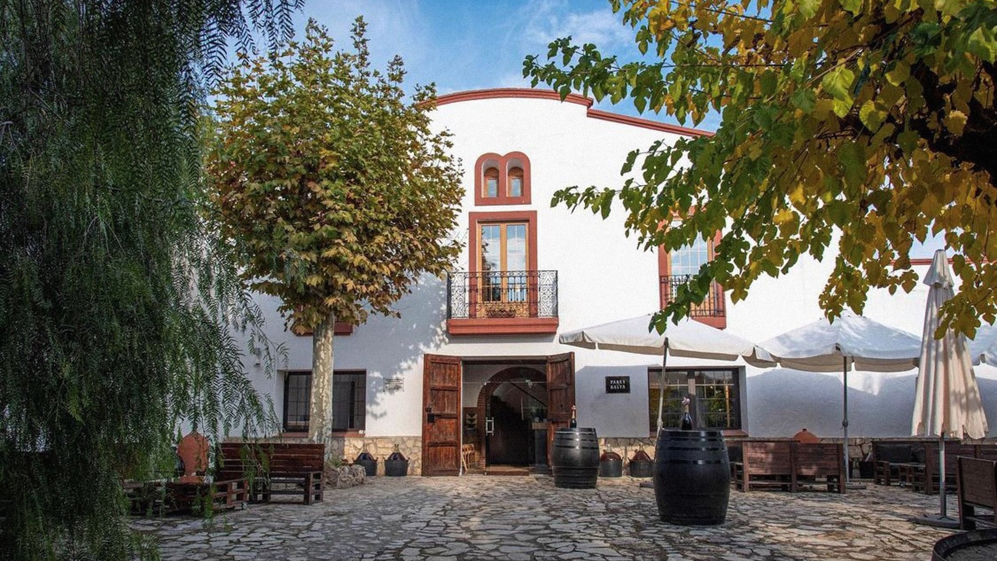 Pares Balta winery facade, white building, open doors, cobblestone courtyard, barrels.