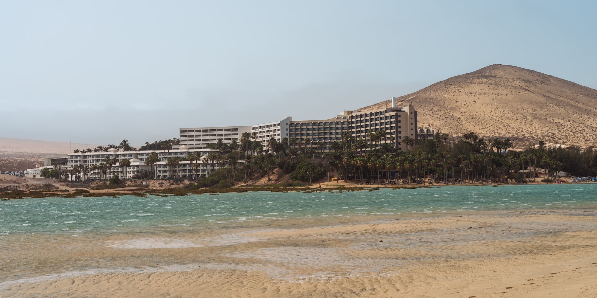 a beach with a building and mountains in the background
