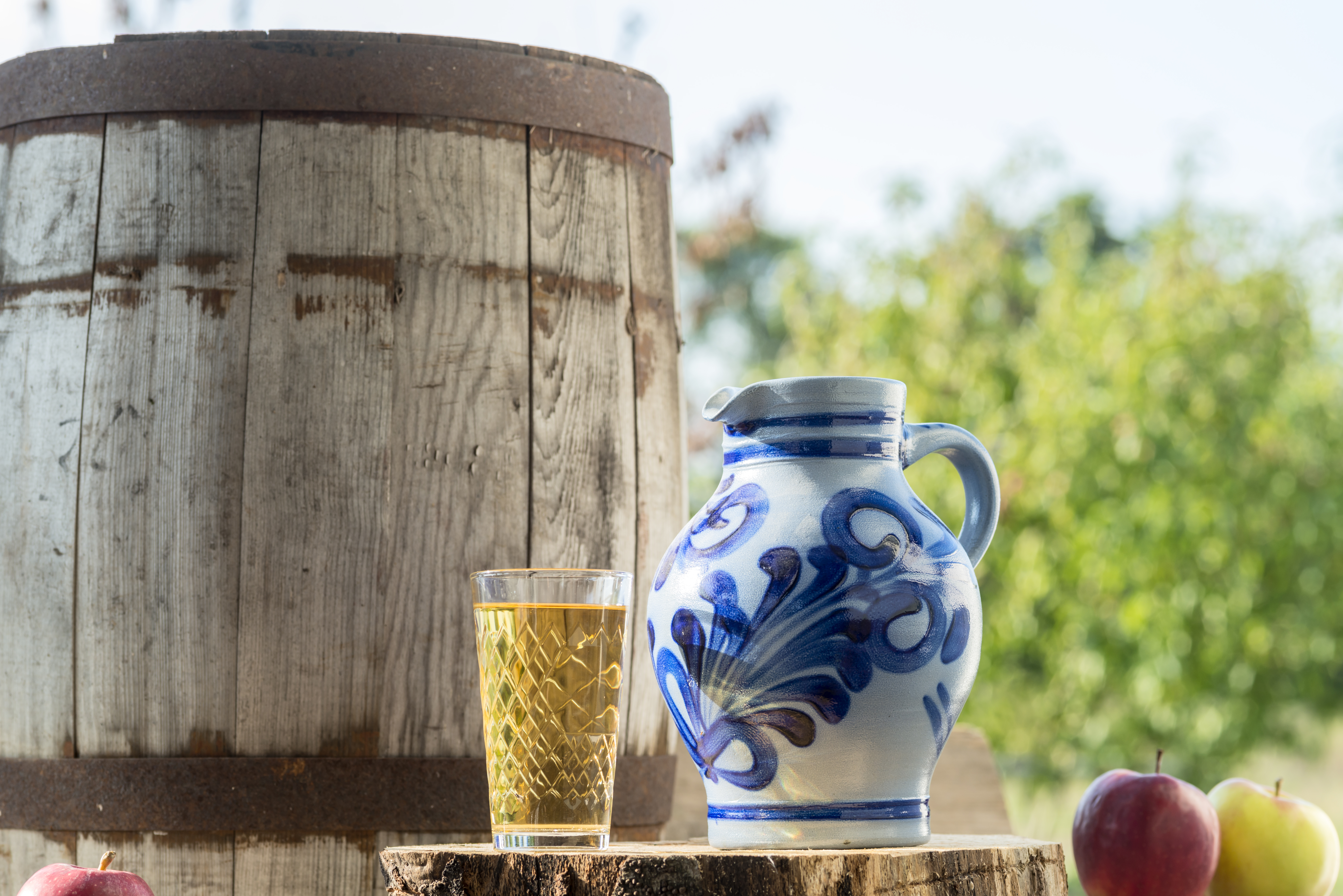 Sidra en vaso, jarra tradicional y manzanas junto a barril de madera rústico.
