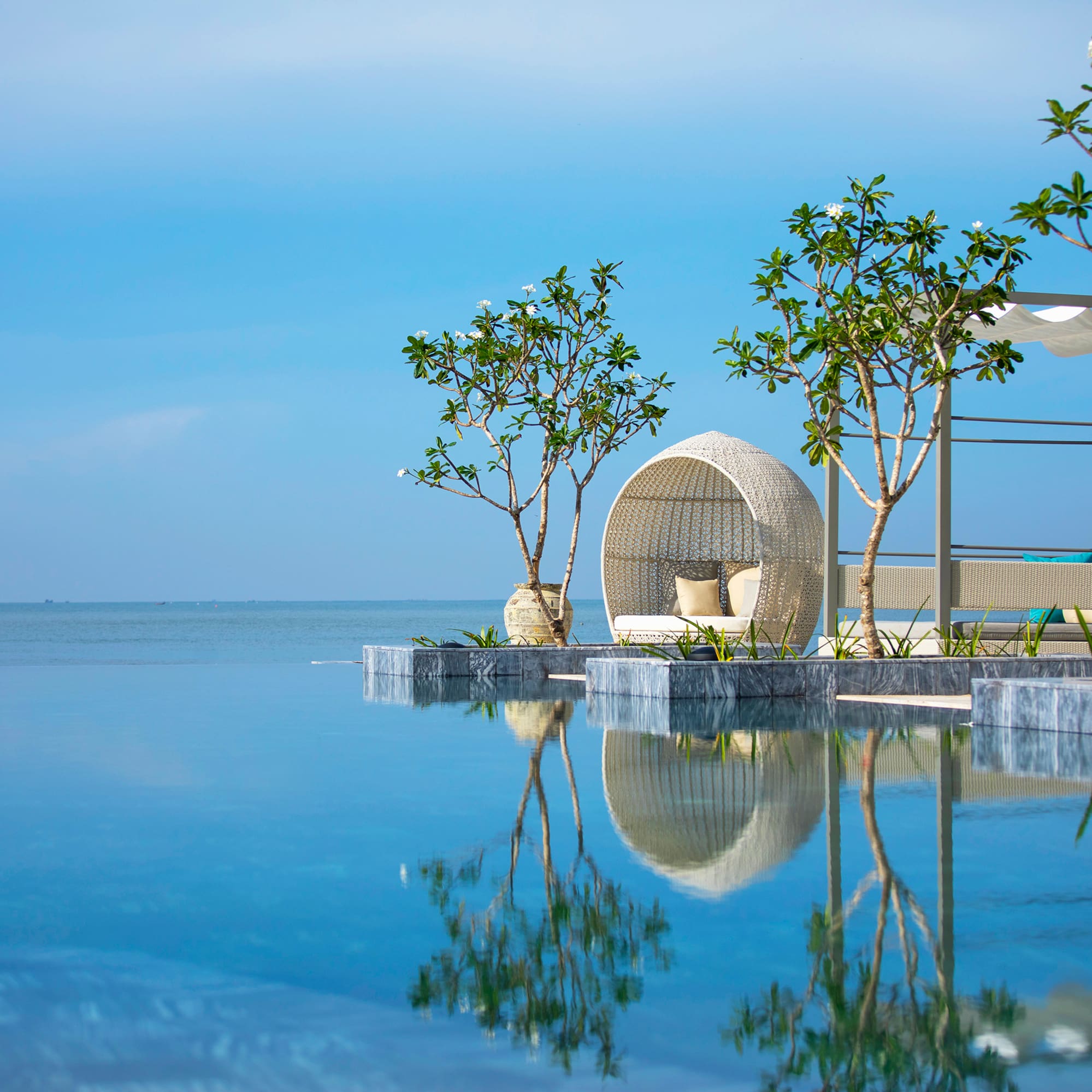 Luxury resort infinity pool with outdoor daybed, tropical trees, ocean view.