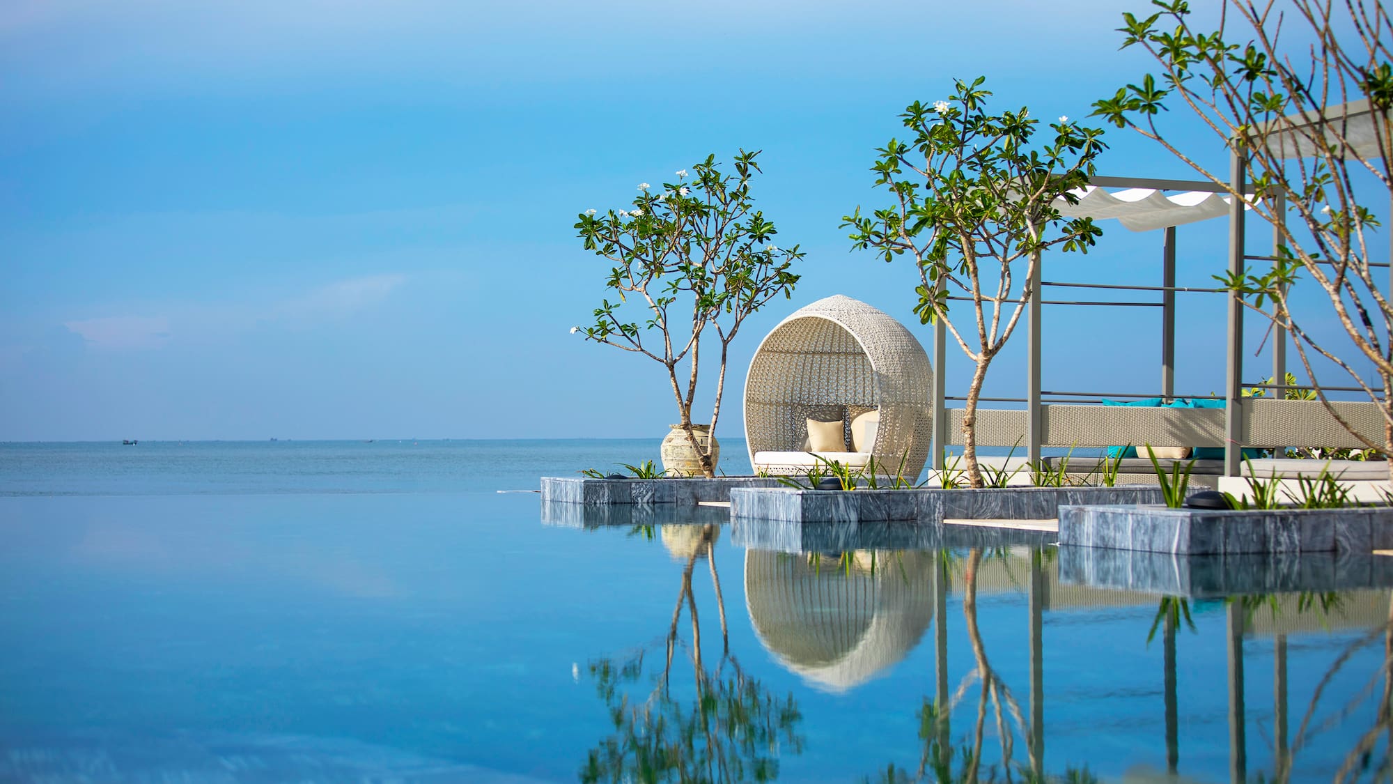 Luxury resort infinity pool with outdoor daybed, tropical trees, ocean view.