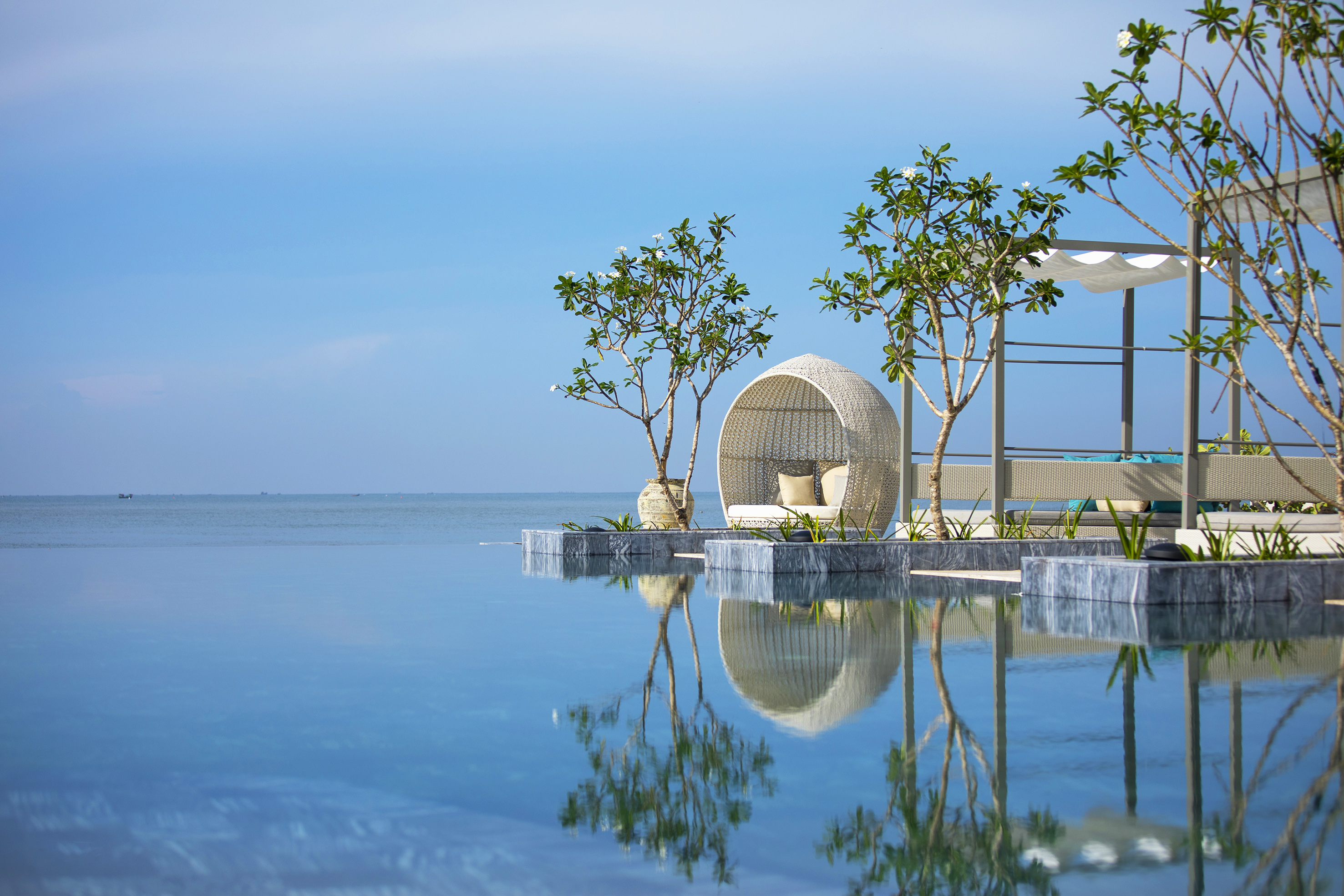 Luxury resort infinity pool with outdoor daybed, tropical trees, ocean view.