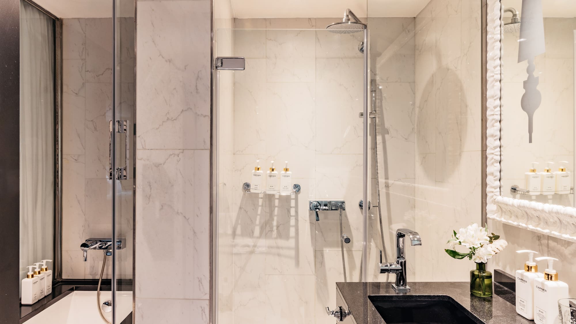 Baño moderno con ducha de cristal, bañera y lavabo negro sobre mármol blanco.