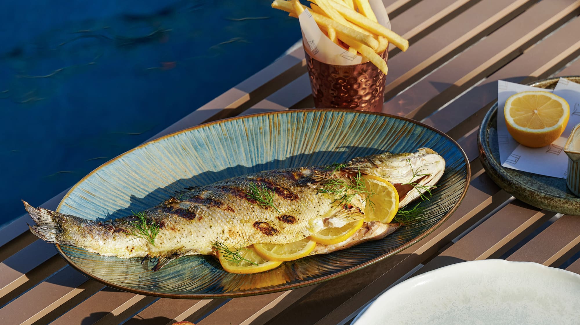 a fish on a plate with lemon slices and potatoes on a table