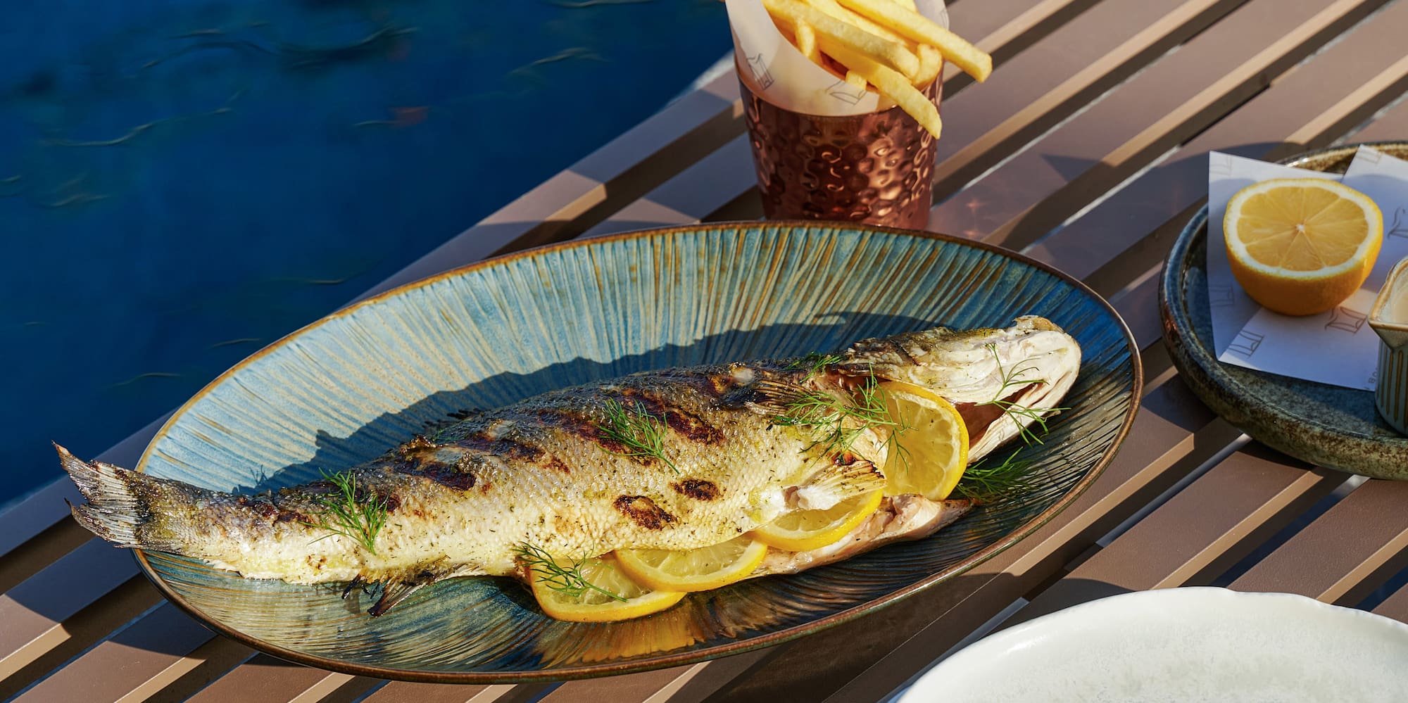 a fish on a plate with lemon slices and potatoes on a table