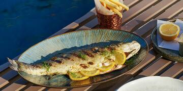 a fish on a plate with lemon slices and potatoes on a table