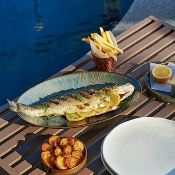 a fish on a plate with lemon slices and potatoes on a table