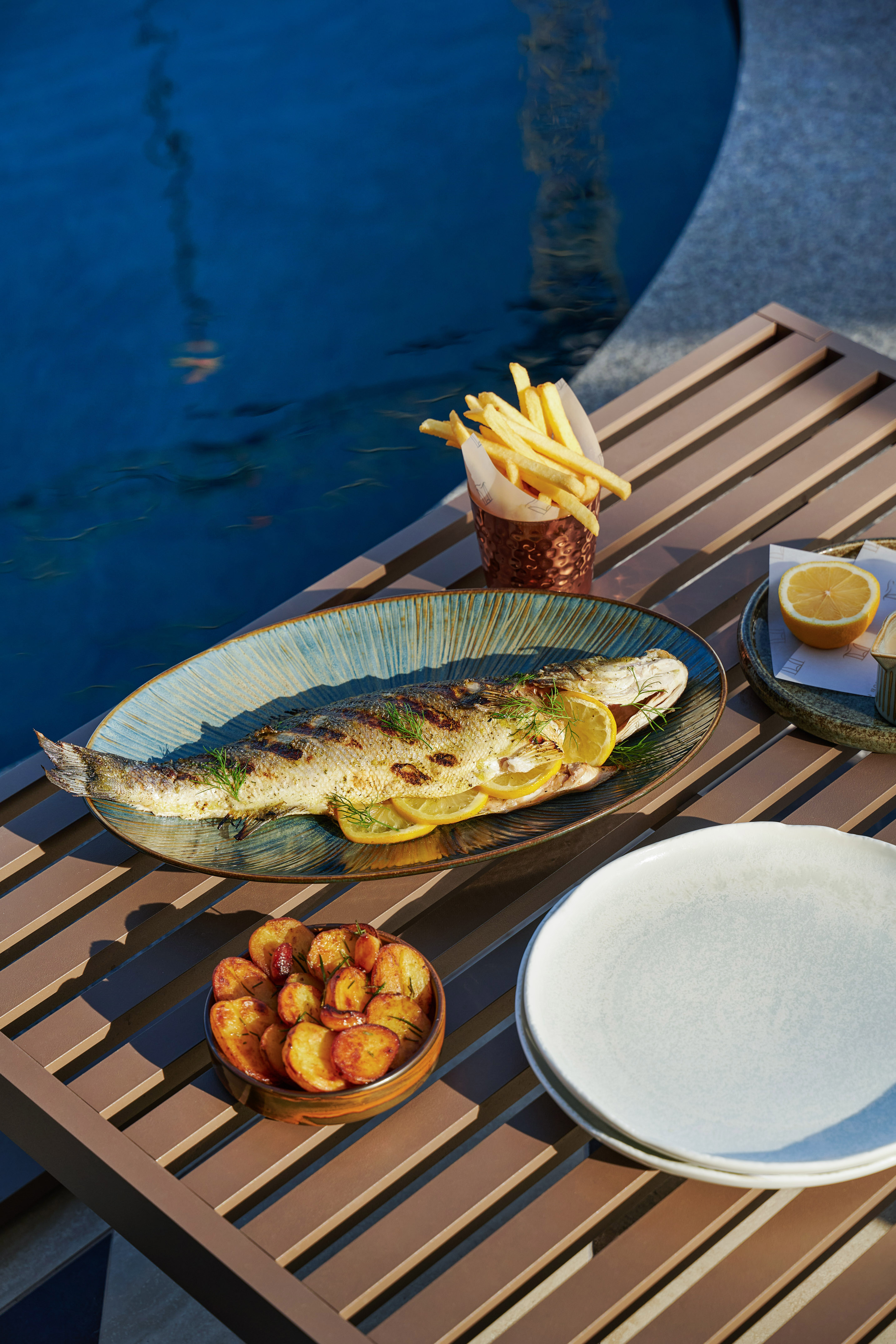 a fish on a plate with lemon slices and potatoes on a table