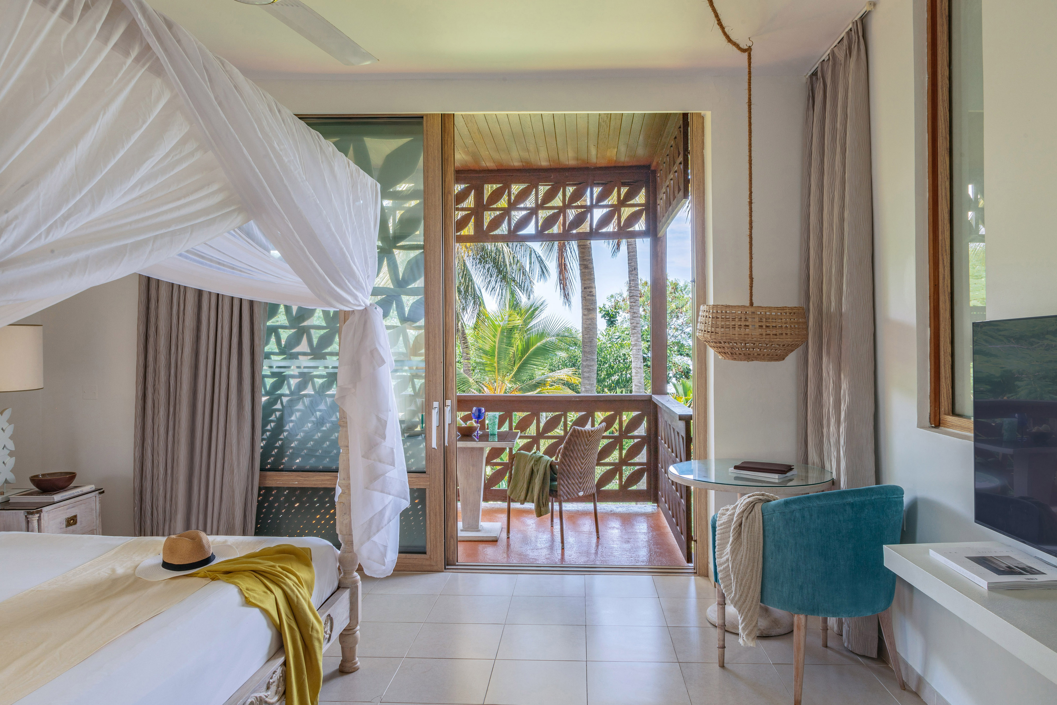 Bright tropical hotel room with canopy bed and balcony facing palm trees.