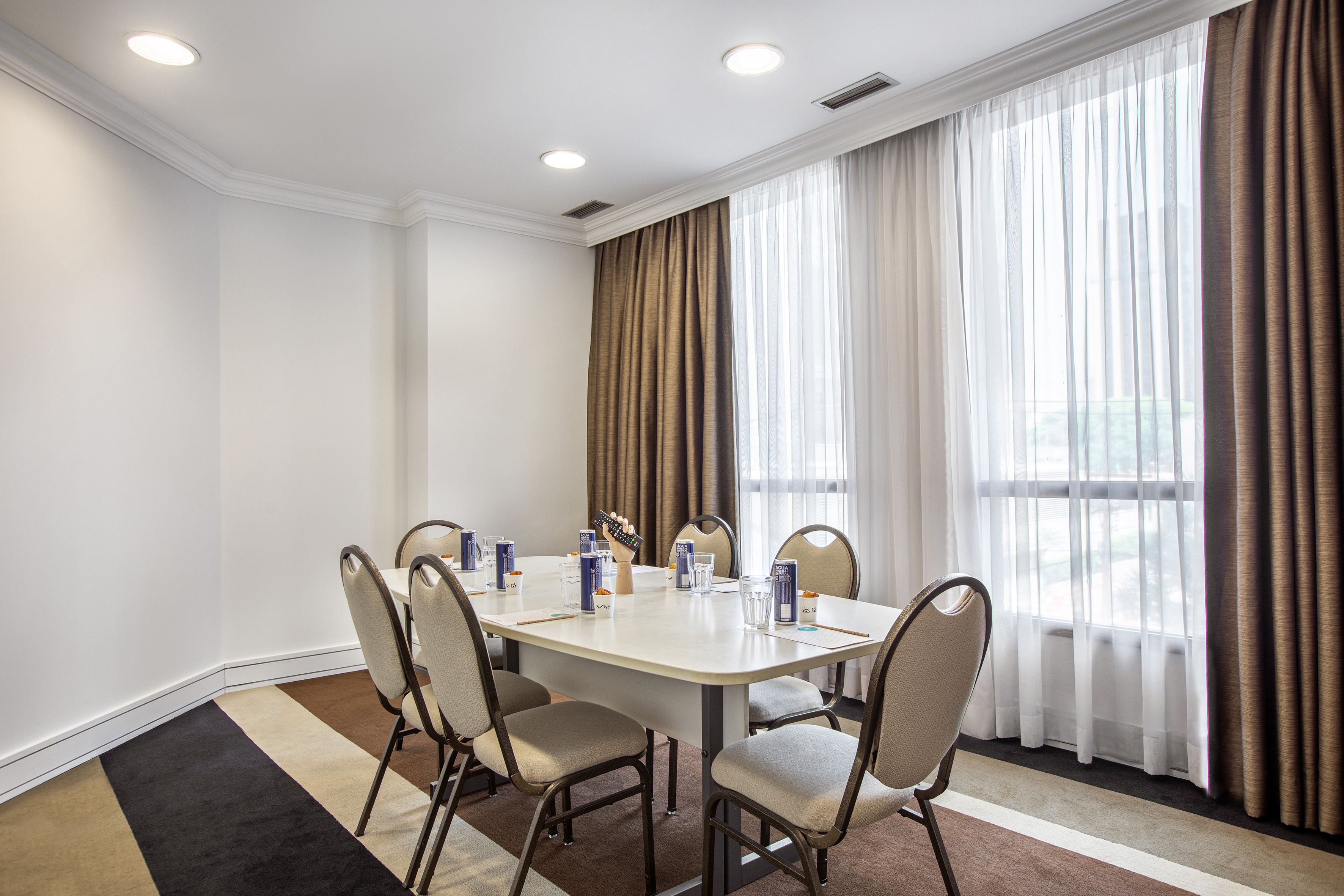 Hotel meeting room with large table, chairs, water bottles, and bright windows.