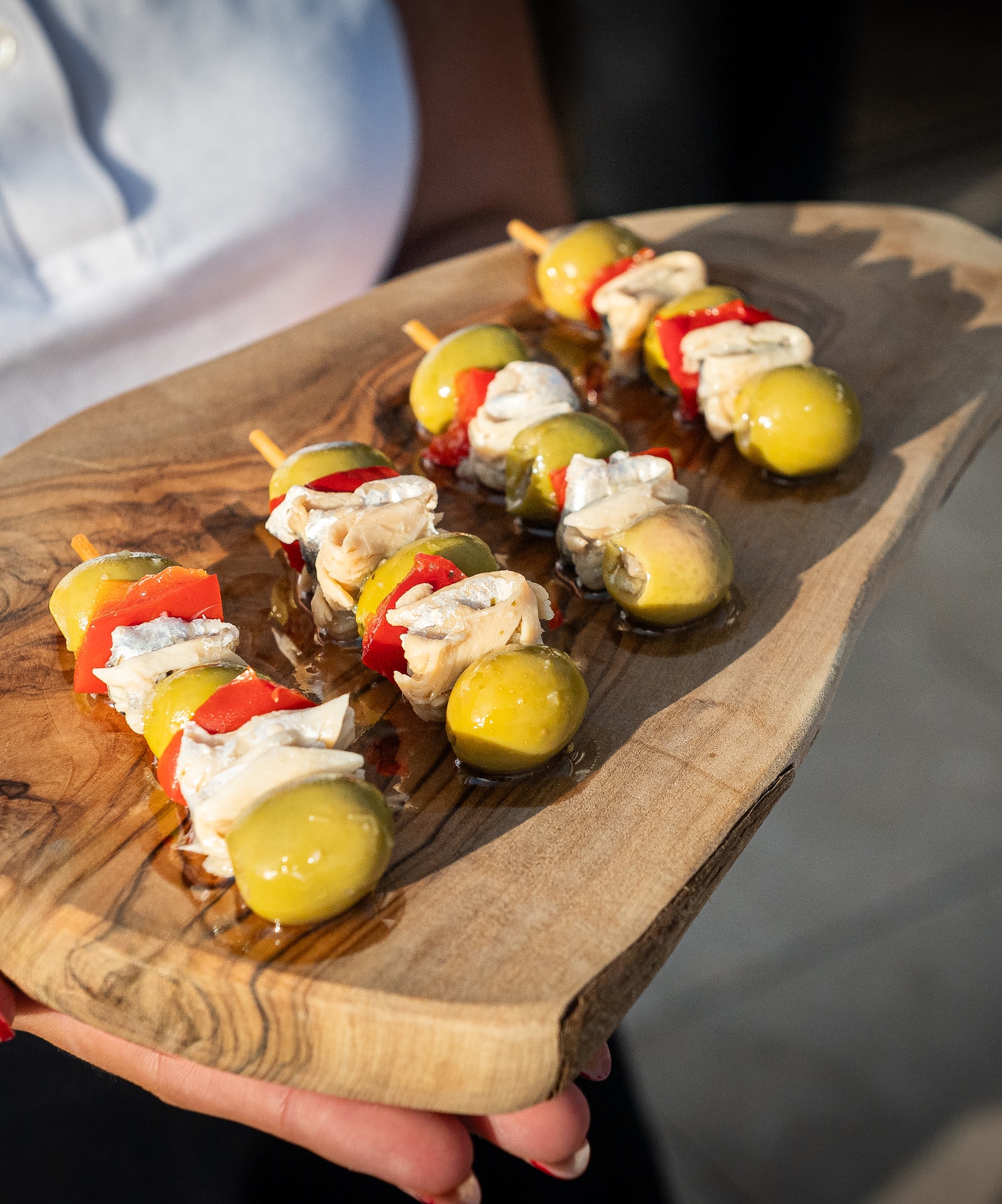 Olive, red pepper, and cheese appetizer skewers on a wooden serving board.