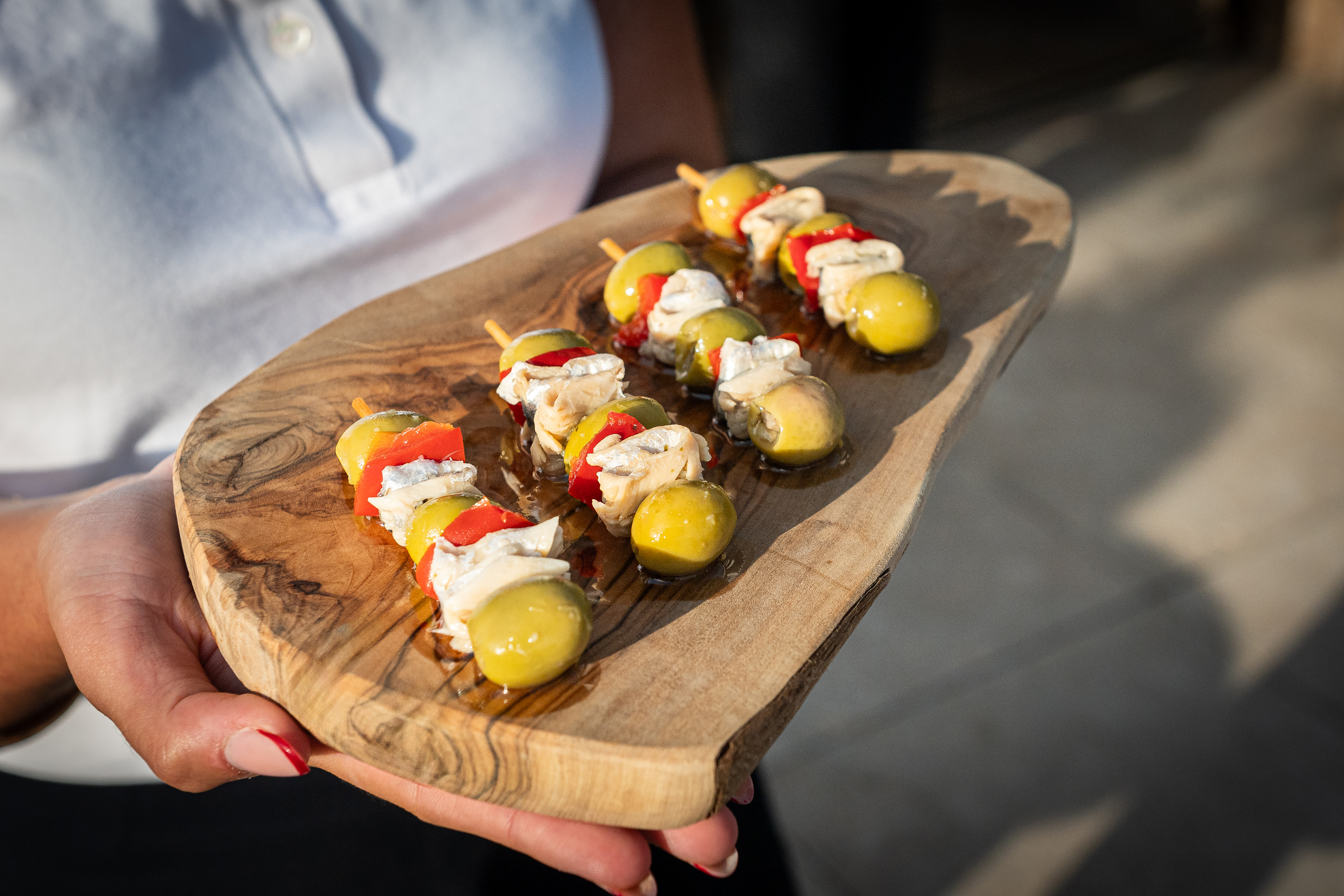 Olive, red pepper, and cheese appetizer skewers on a wooden serving board.
