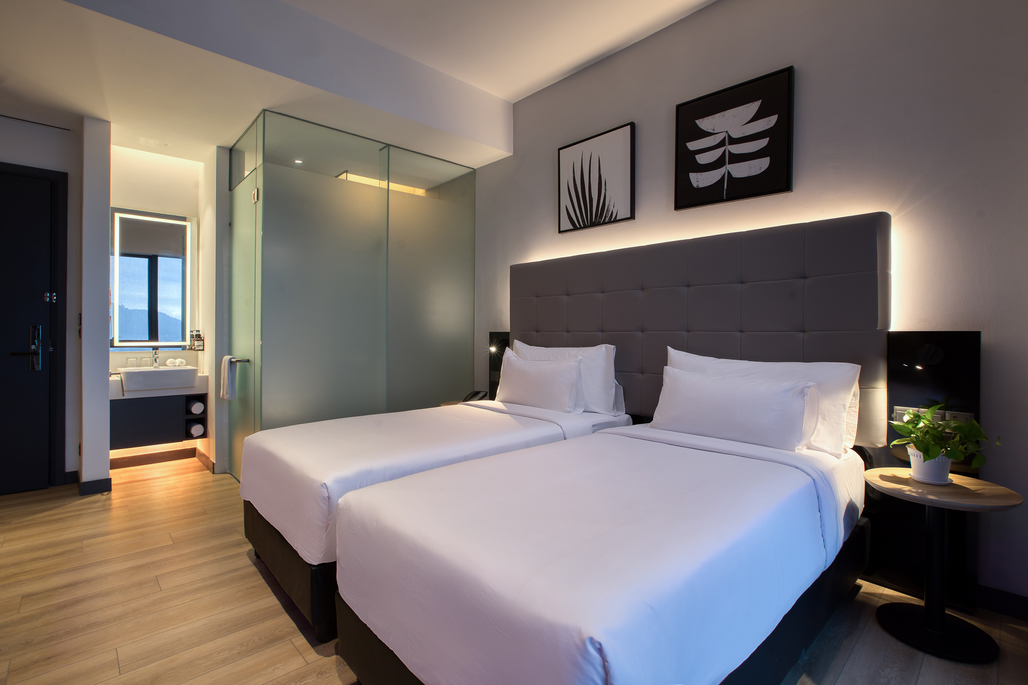 Modern twin hotel room with two beds, gray headboard, and integrated bathroom.