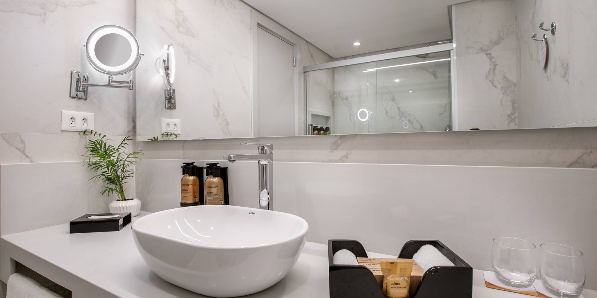 Modern hotel bathroom vanity with vessel sink, marble walls, and spa toiletries.