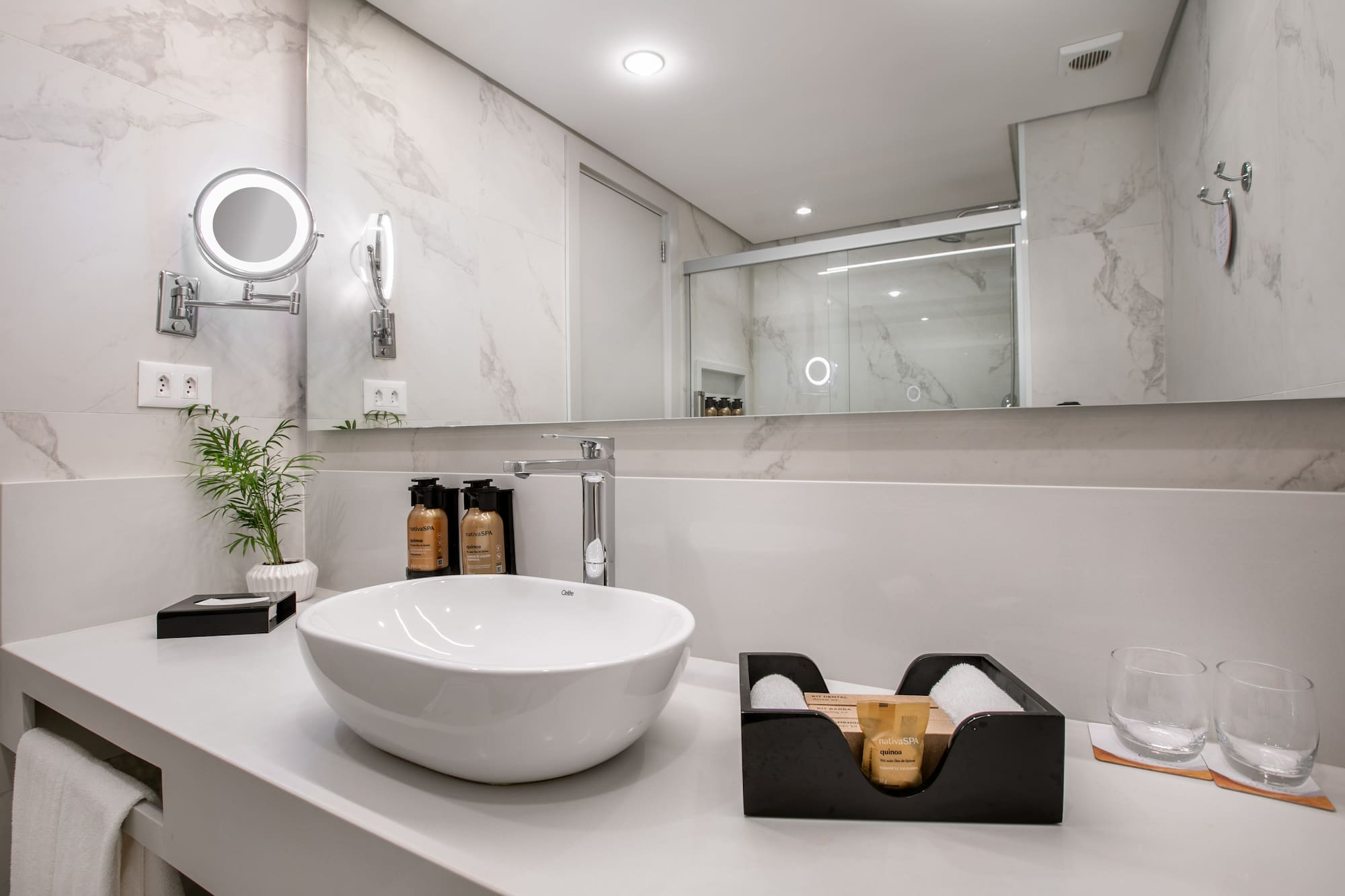 Modern bathroom vanity, white vessel sink, illuminated mirror, marble tiles.