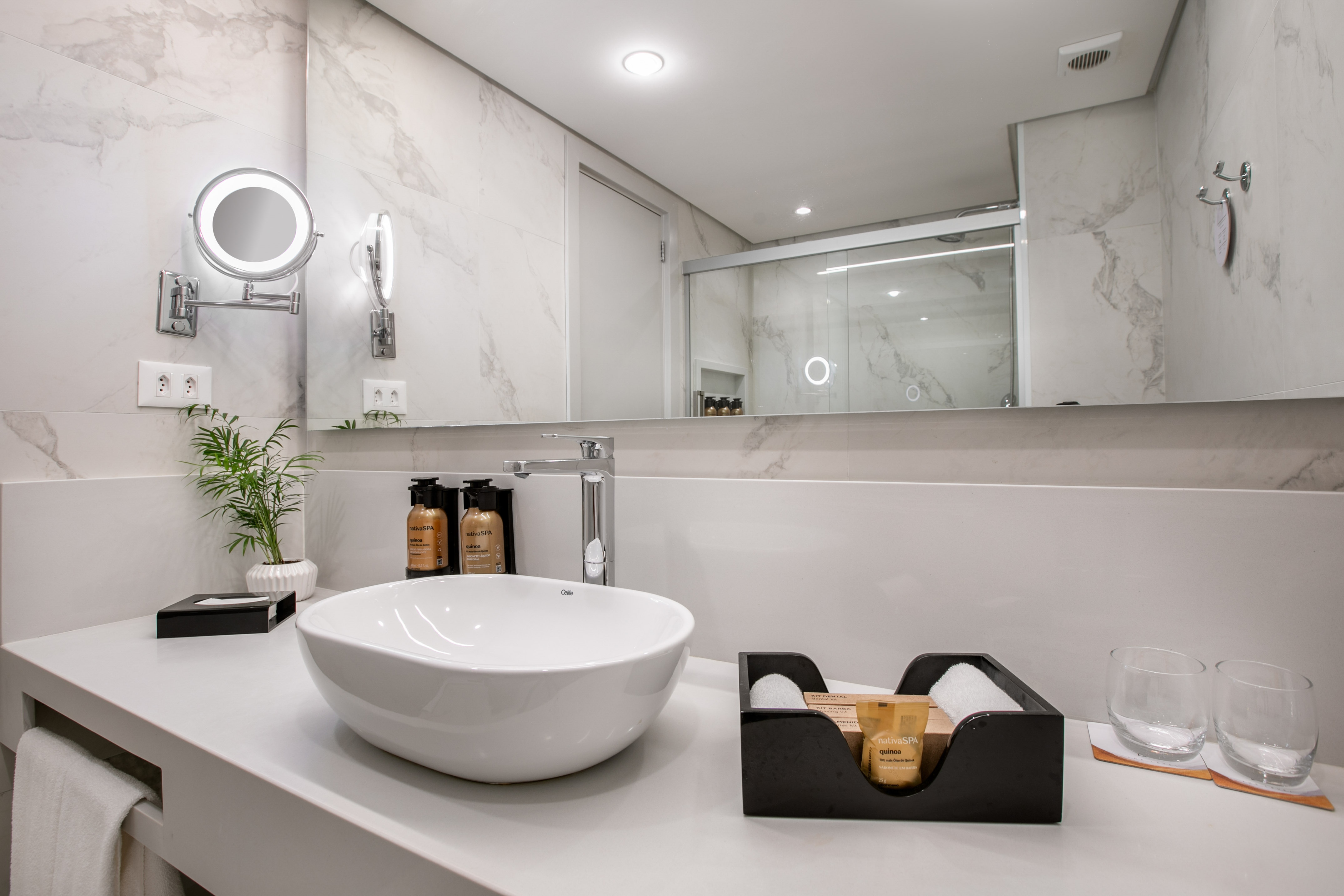 Modern bathroom vanity, white vessel sink, illuminated mirror, marble tiles.