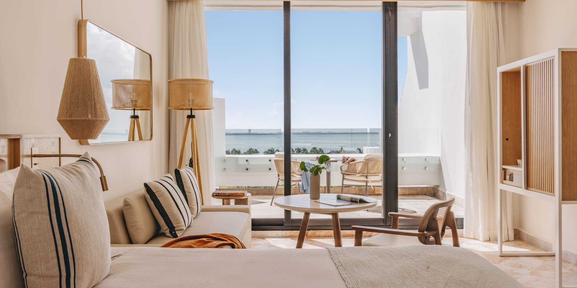 Bright hotel suite with ocean view, balcony, and contemporary coastal decor.