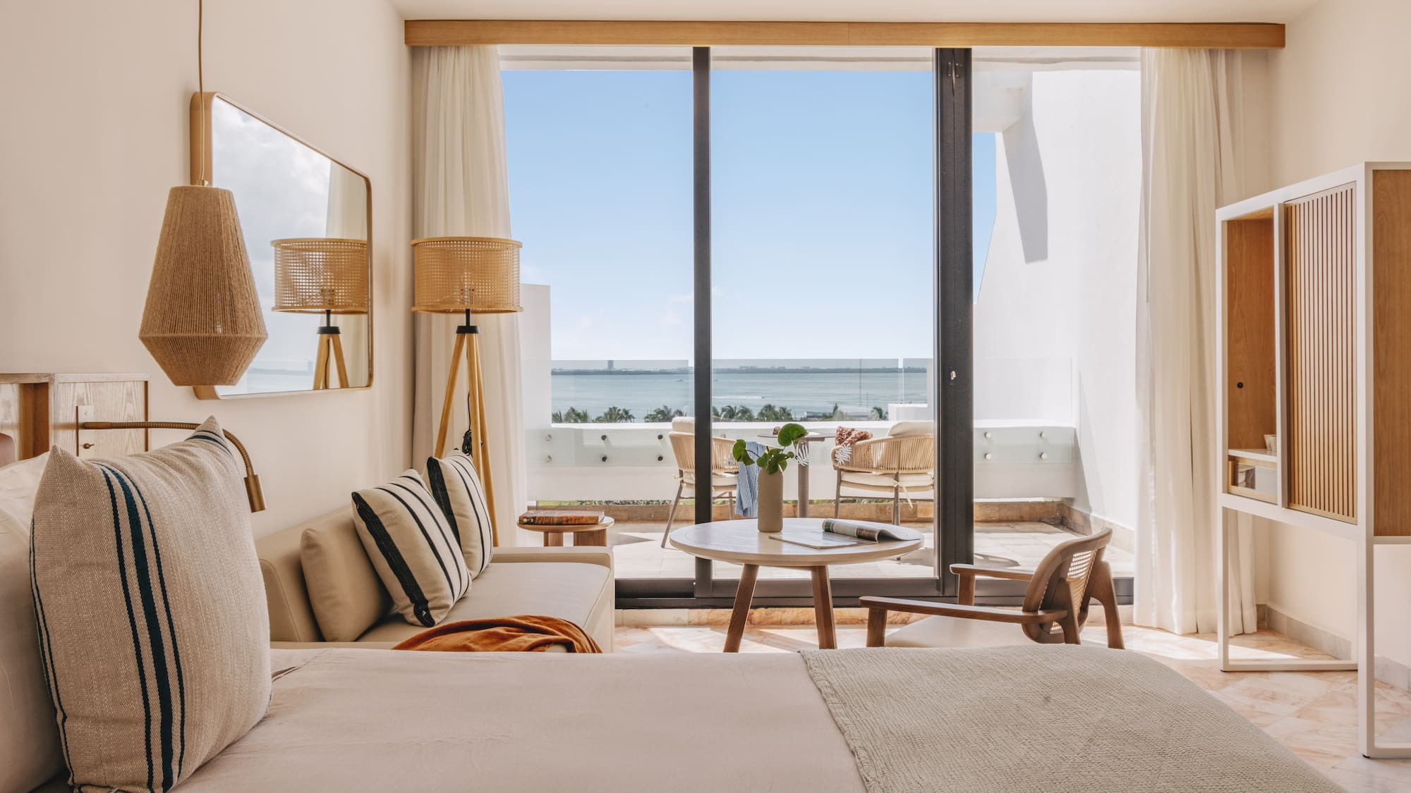 Bright hotel suite with ocean view, balcony, and contemporary coastal decor.