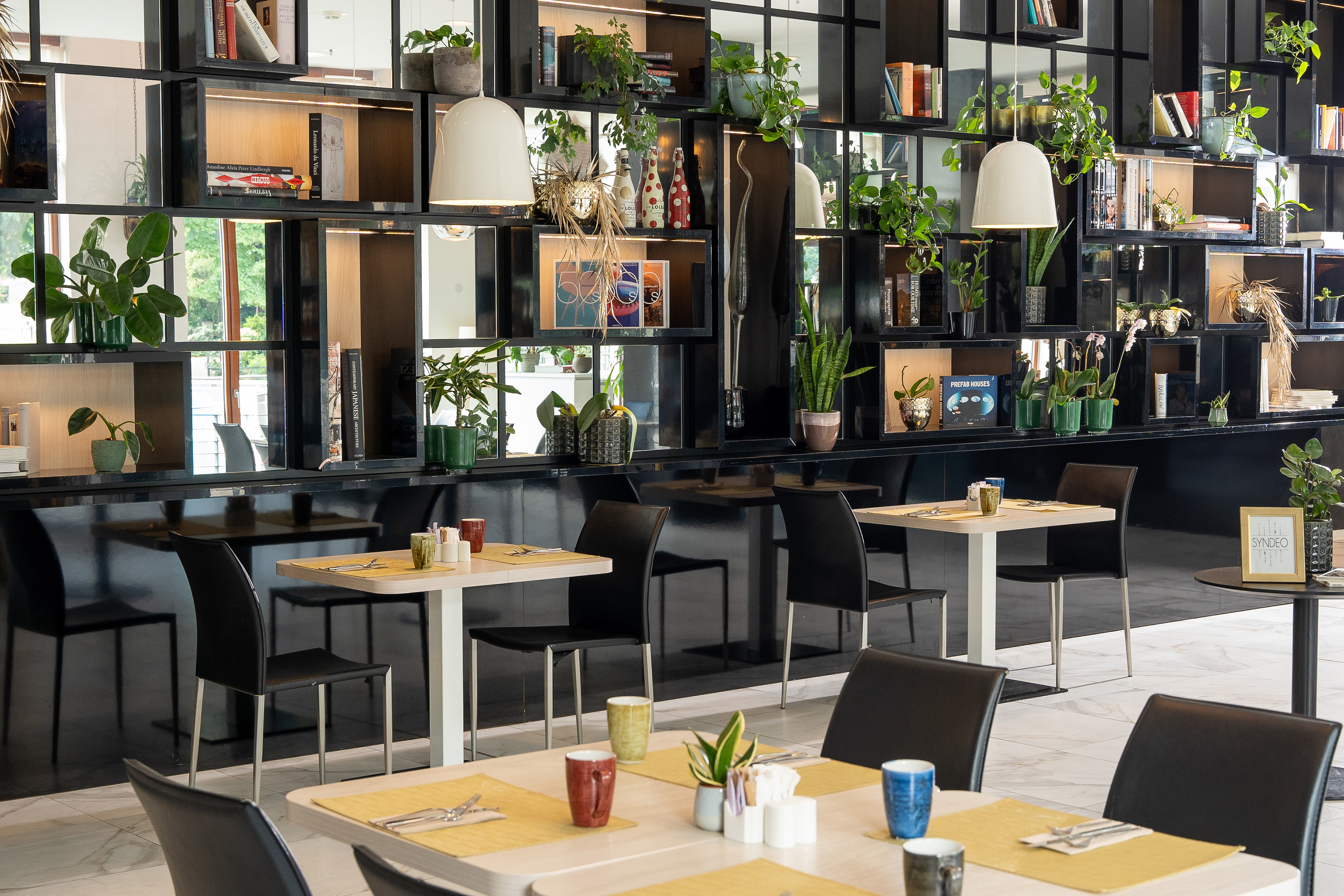 Modern cafe with black shelving, potted plants, books, and set dining tables.