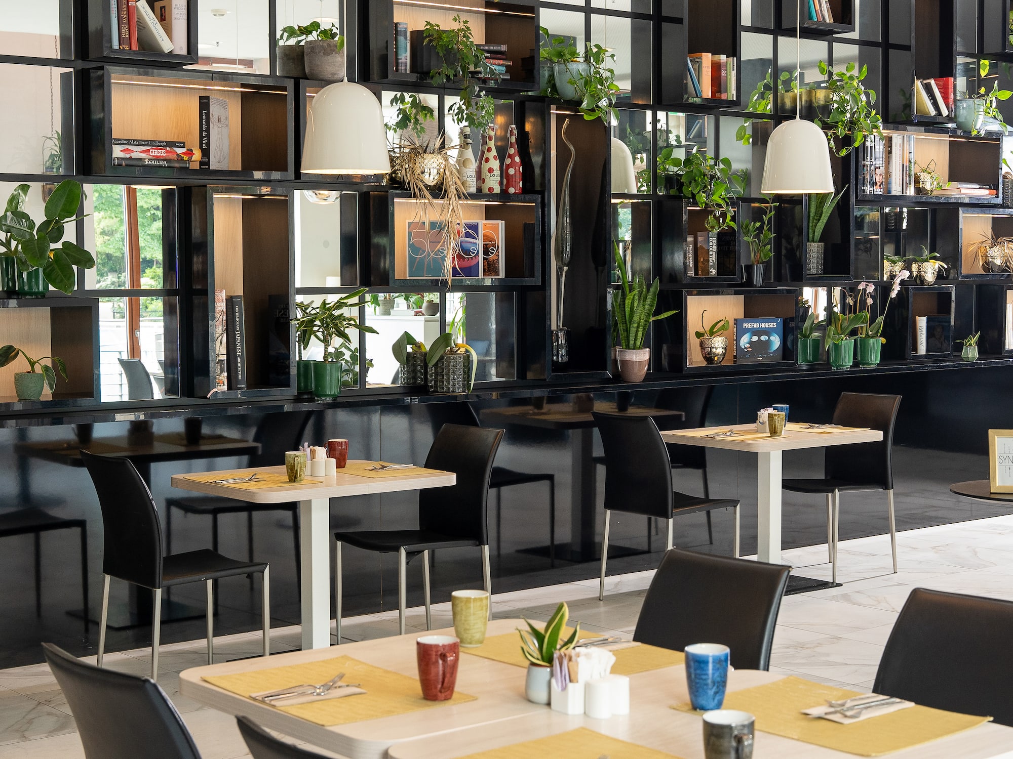 Modern cafe with black shelving, potted plants, books, and set dining tables.