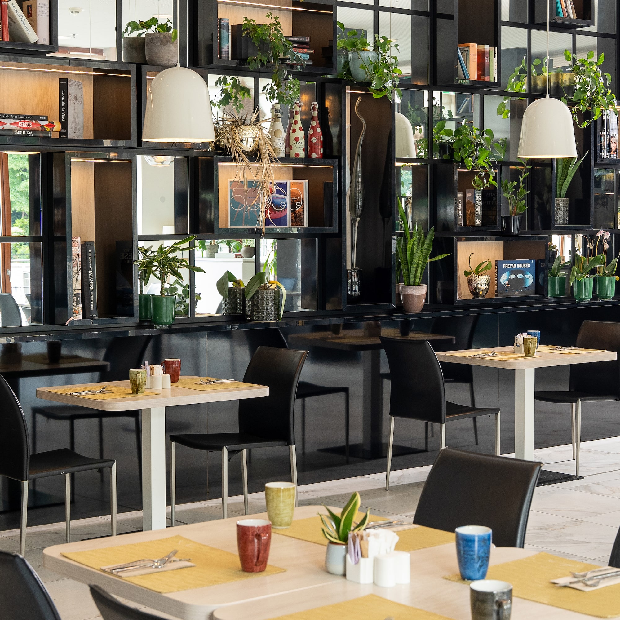Modern cafe with black shelving, potted plants, books, and set dining tables.