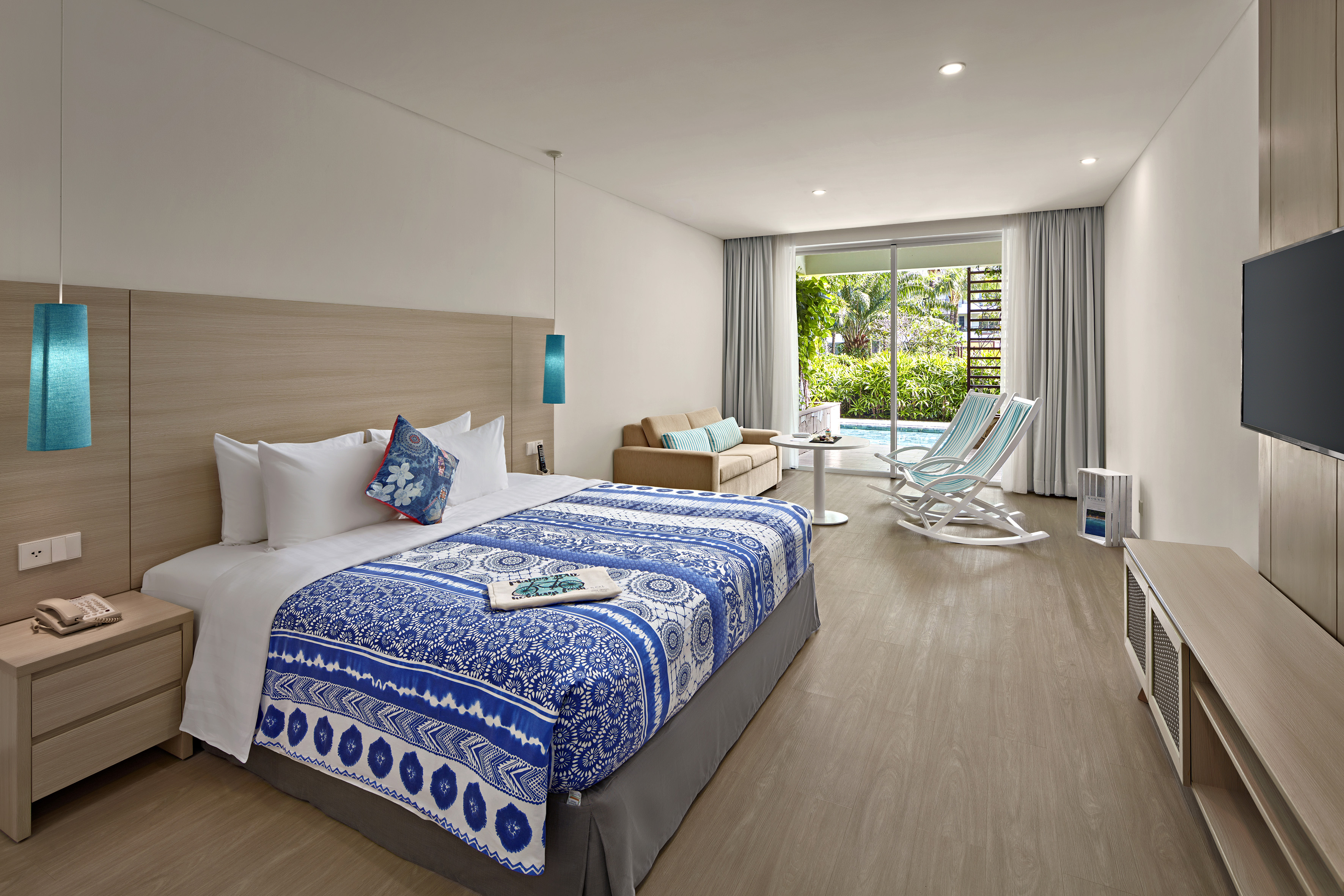 Tropical hotel room with patterned bed, lounge, and pool view patio.